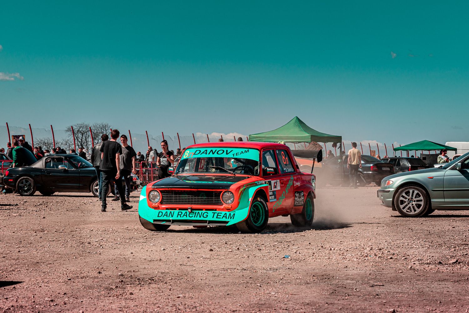 Wide view of an automotive gathering featuring classic cars, spectators and dynamic event energy under clear skies in Bulgaria.