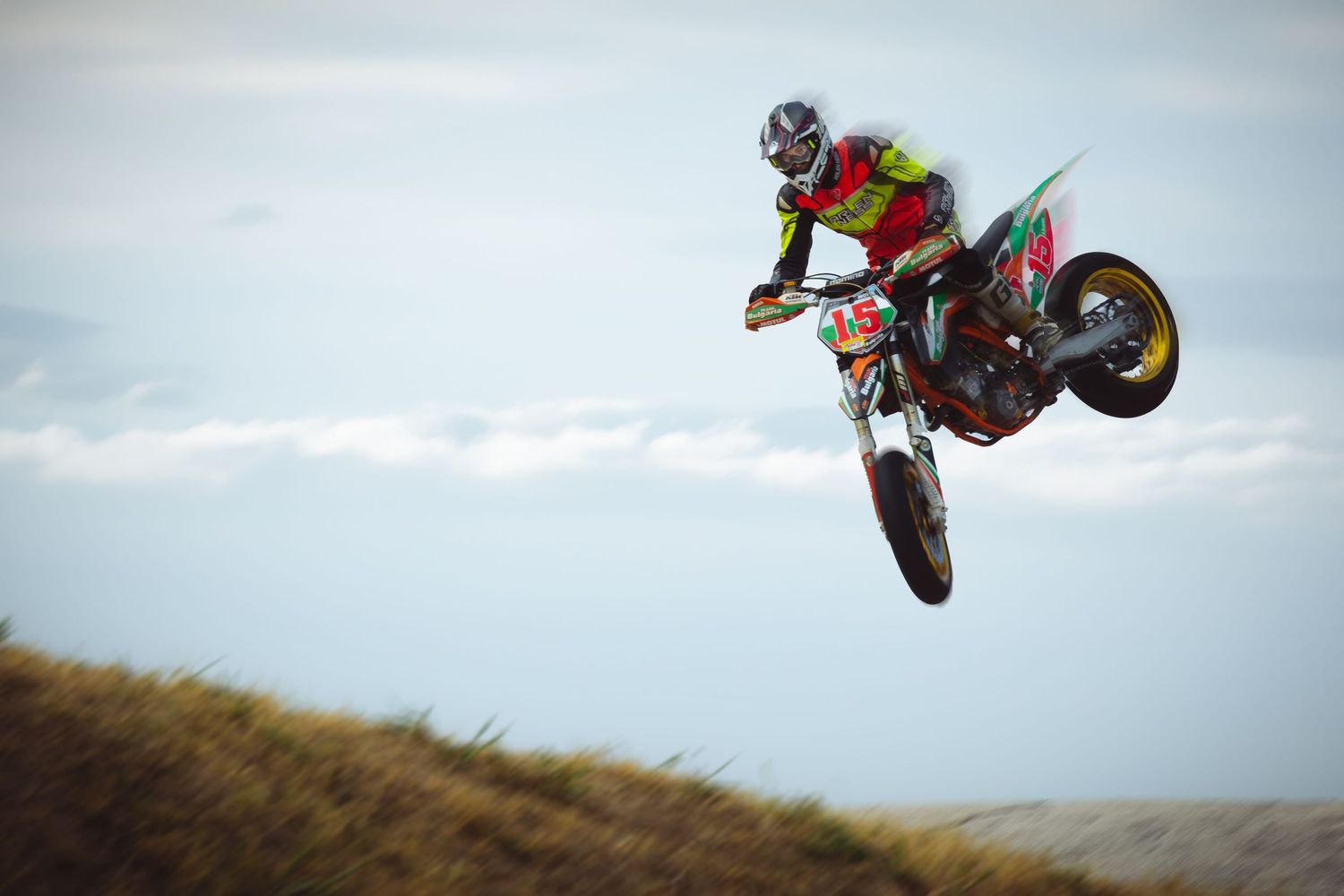 Motocross rider performing high jump over dirt track during race – sports photography in Bulgaria.