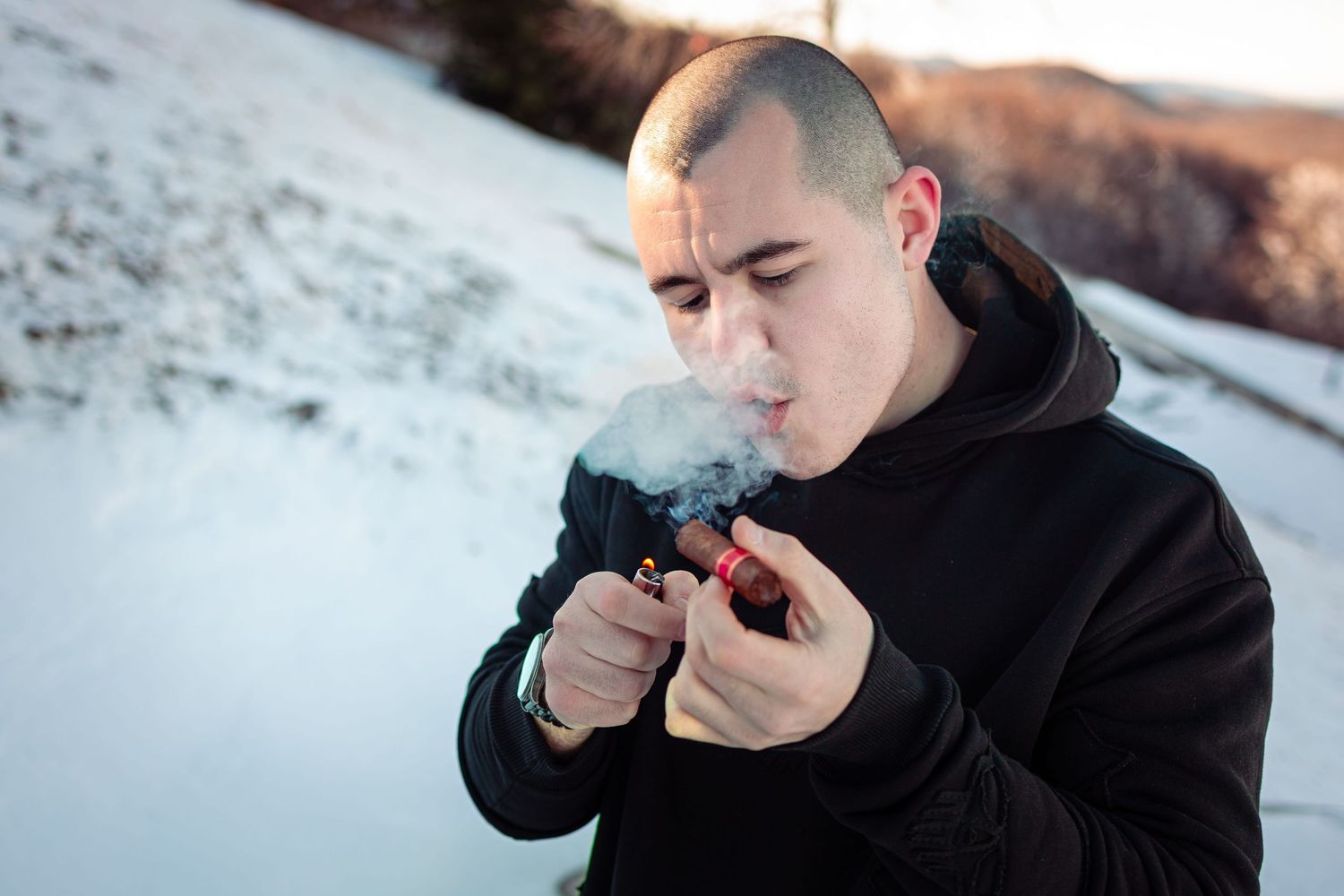 Close-up portrait of a man lighting a cigar in a snowy mountain setting during golden hour – outdoor portrait photography in Bulgaria.