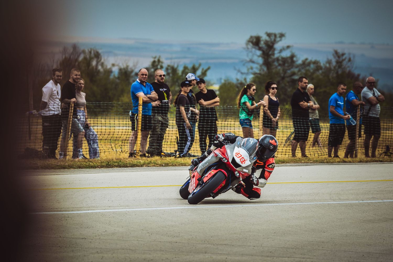 Motorcycle racer leaning into corner during road race with spectators – sports photography in Bulgaria.