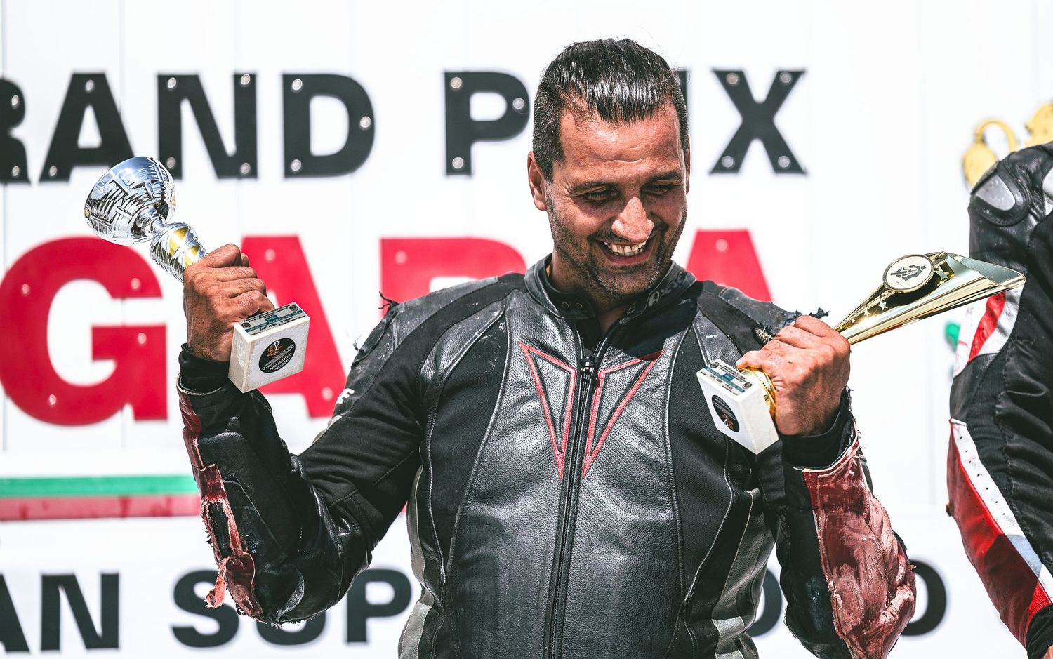 Motorsport rider celebrating victory with trophy on podium – sports photography in Bulgaria.