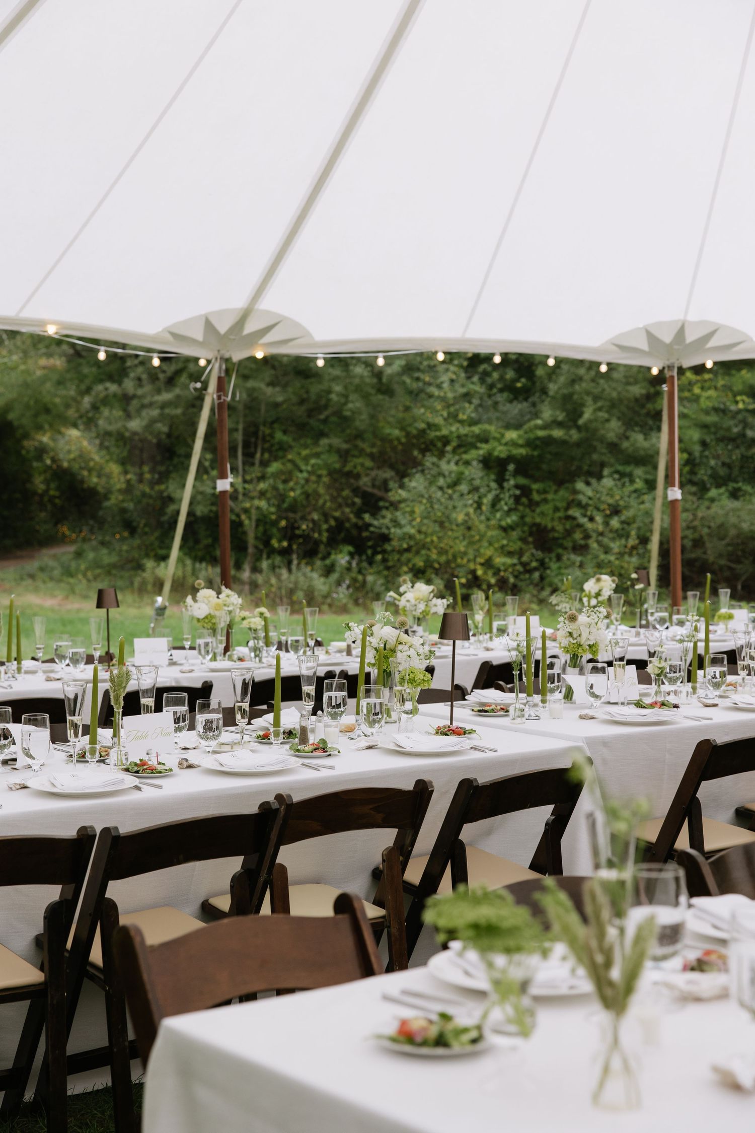 An elegant outdoor wedding reception setup with white tent, tables, and simple floral centerpieces.