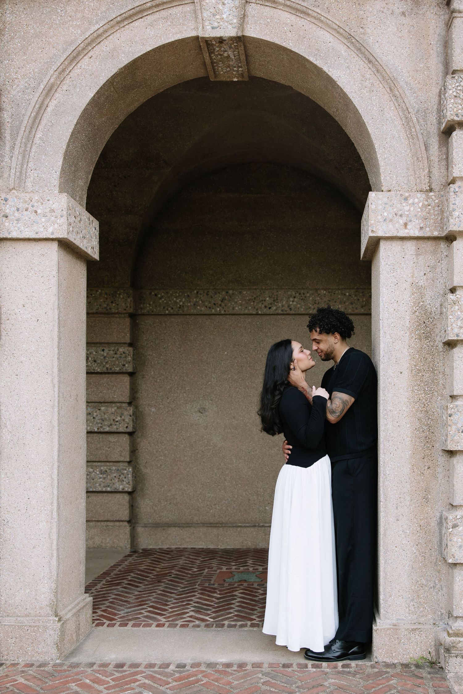 A romantic moment captured under a stone archway with brick flooring.