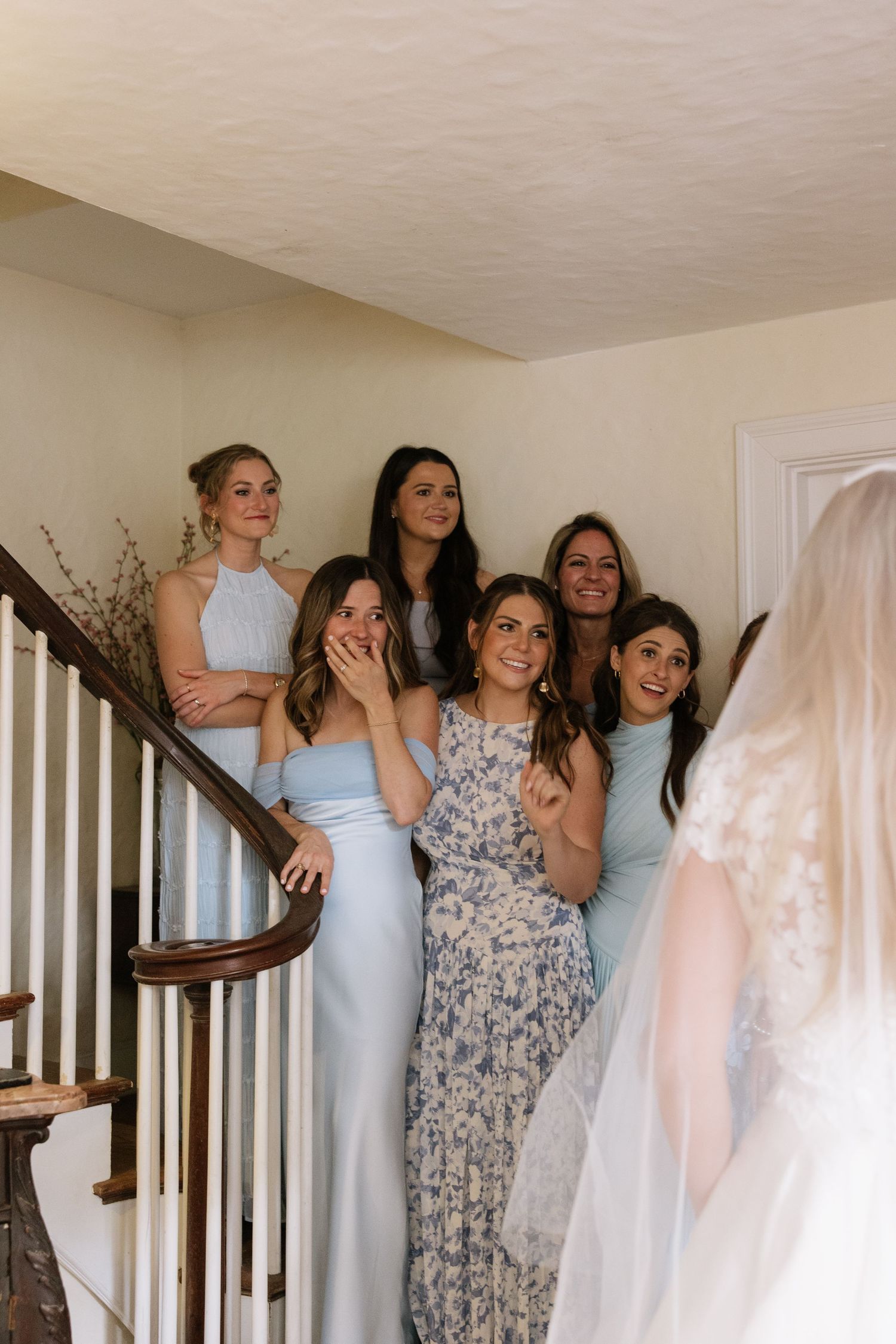 Wedding party members in light blue and floral dresses gather on a staircase.
