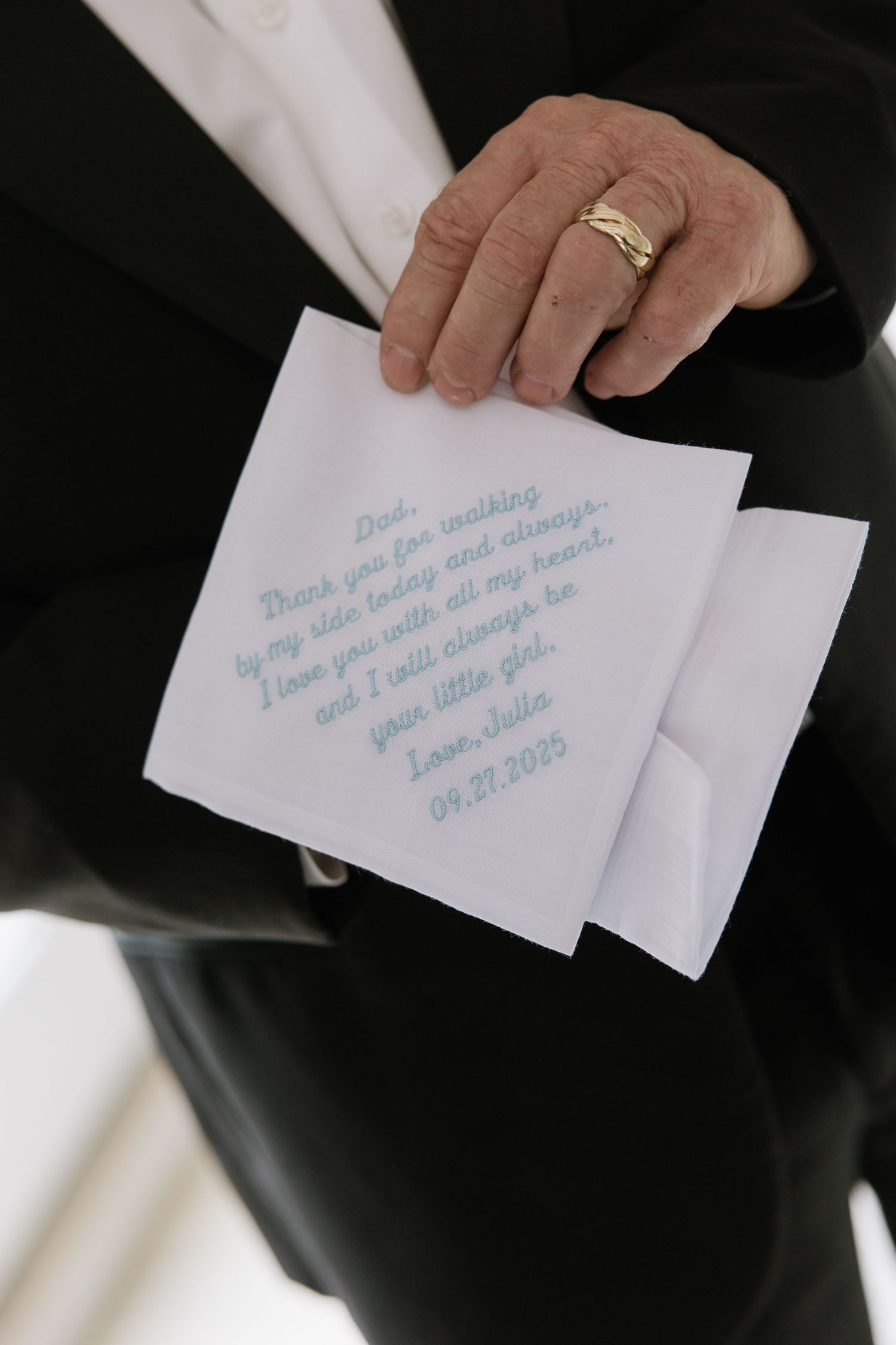 A close-up of hands holding a handwritten note with blue text against formal attire.