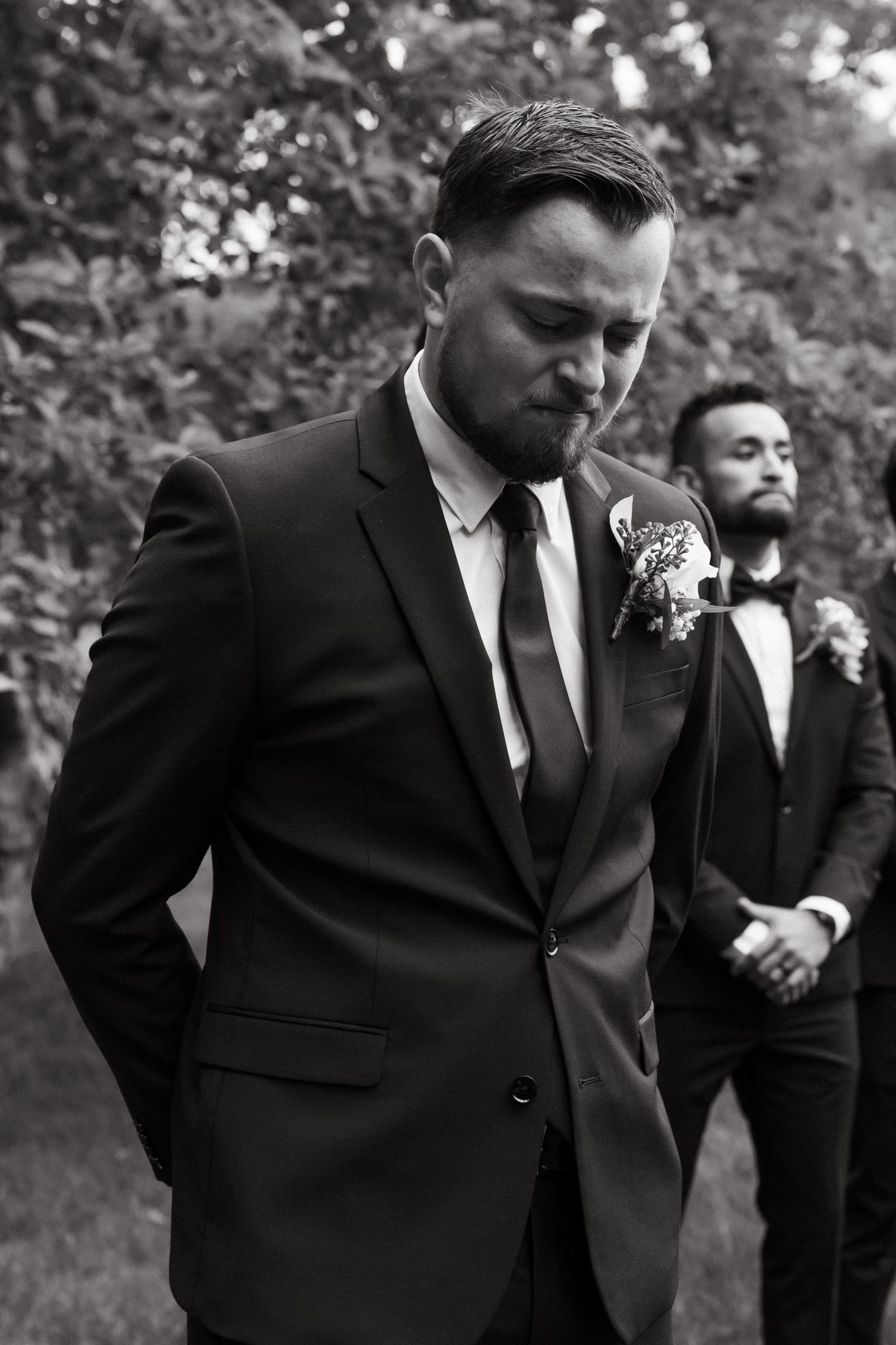 A groom in a dark suit and tie looks down thoughtfully before the ceremony.