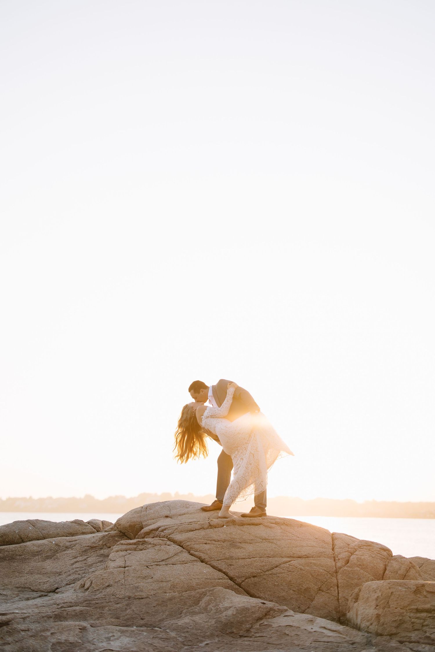 Two figures exploring coastal rocks at sunset with warm glowing light.