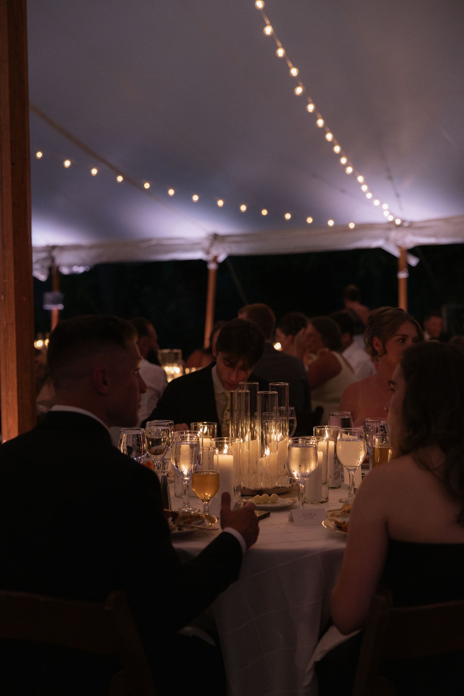 Candlelit wedding reception tables under a tent with twinkling lights overhead.
