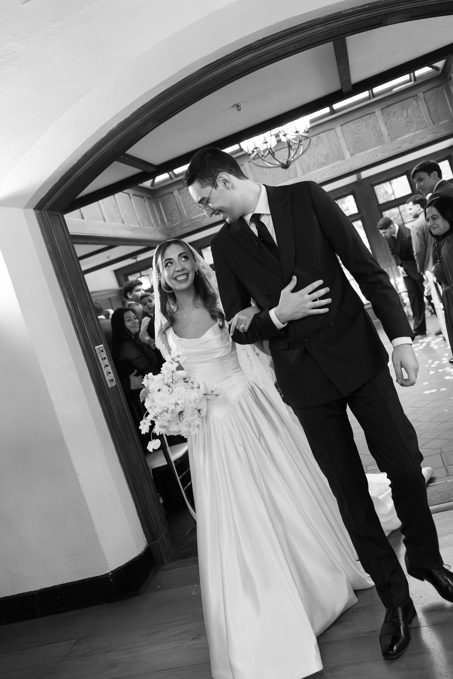 A black and white photo series showing a couple walking through an arched hallway at their wedding.