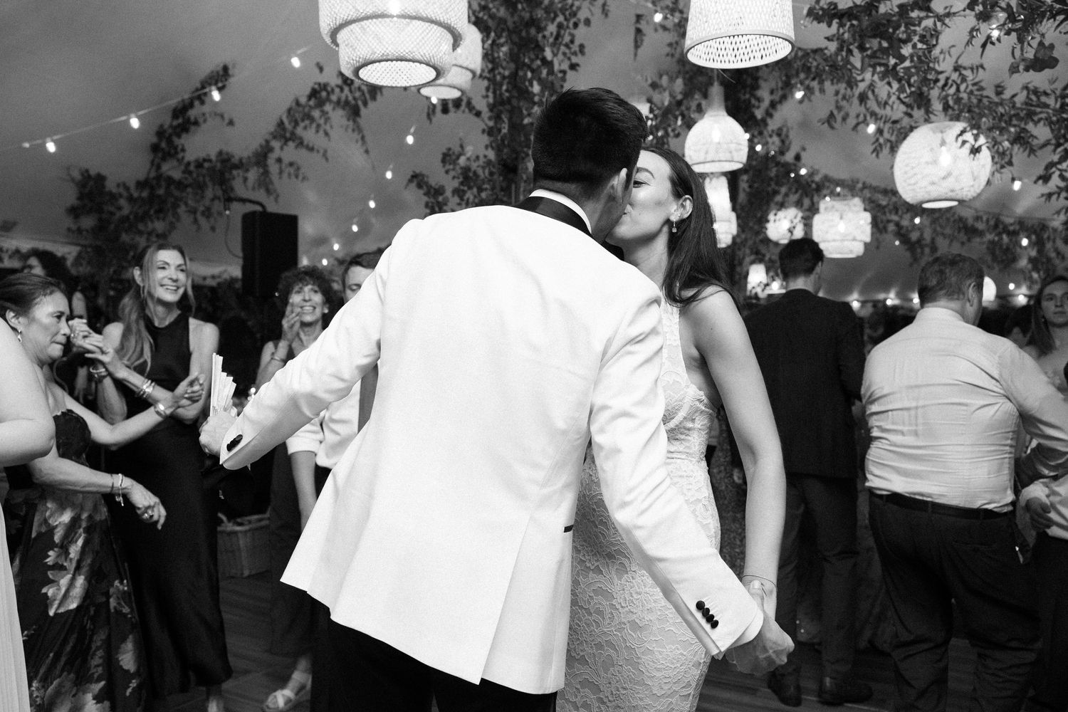 Couple shares a romantic kiss on the dance floor at an elegant outdoor wedding reception in black and white.