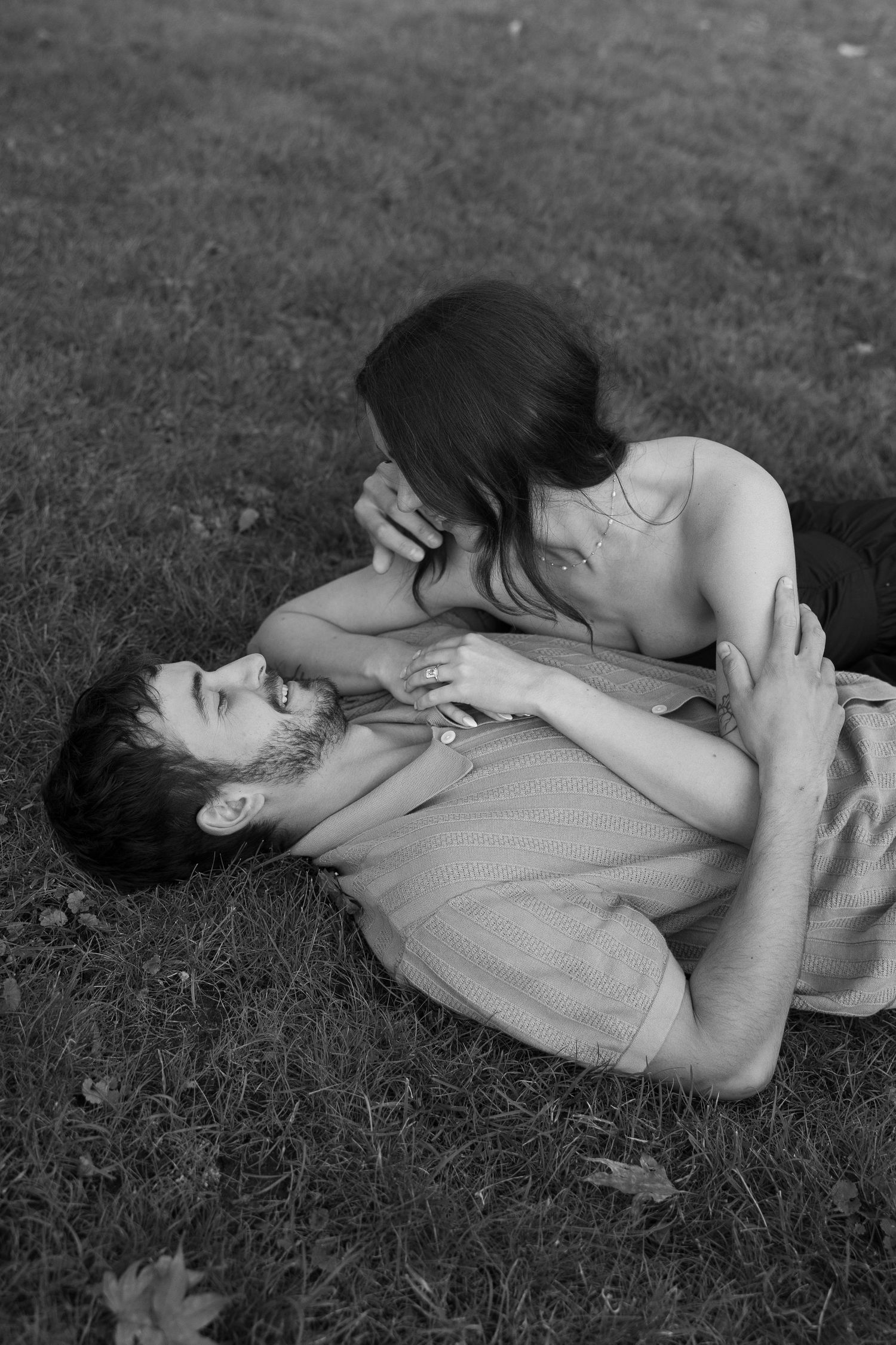 Two people share an intimate moment lying in the grass, captured in black and white.