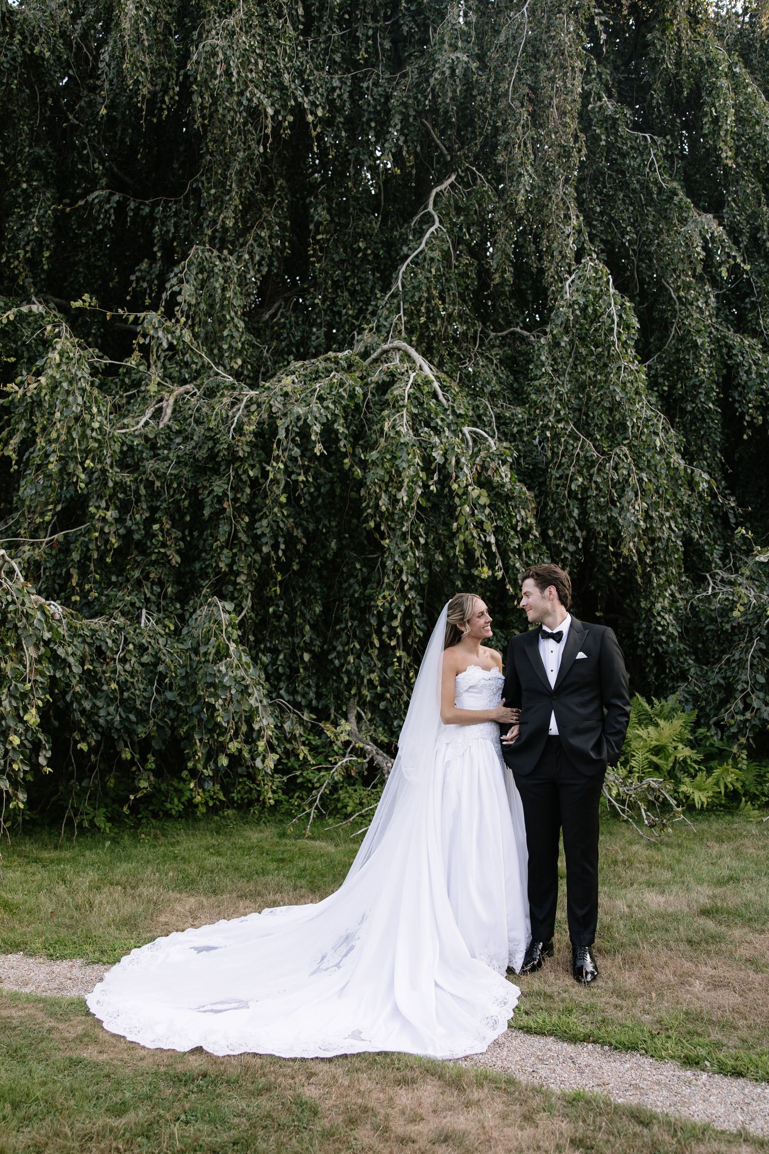 Wedding portraits captured against a backdrop of weeping willow trees in a garden setting.