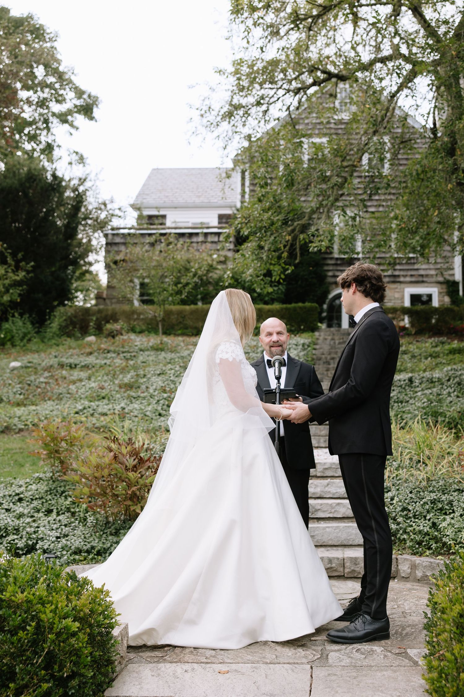 Wedding ceremony takes place on stone path with classic house in background.