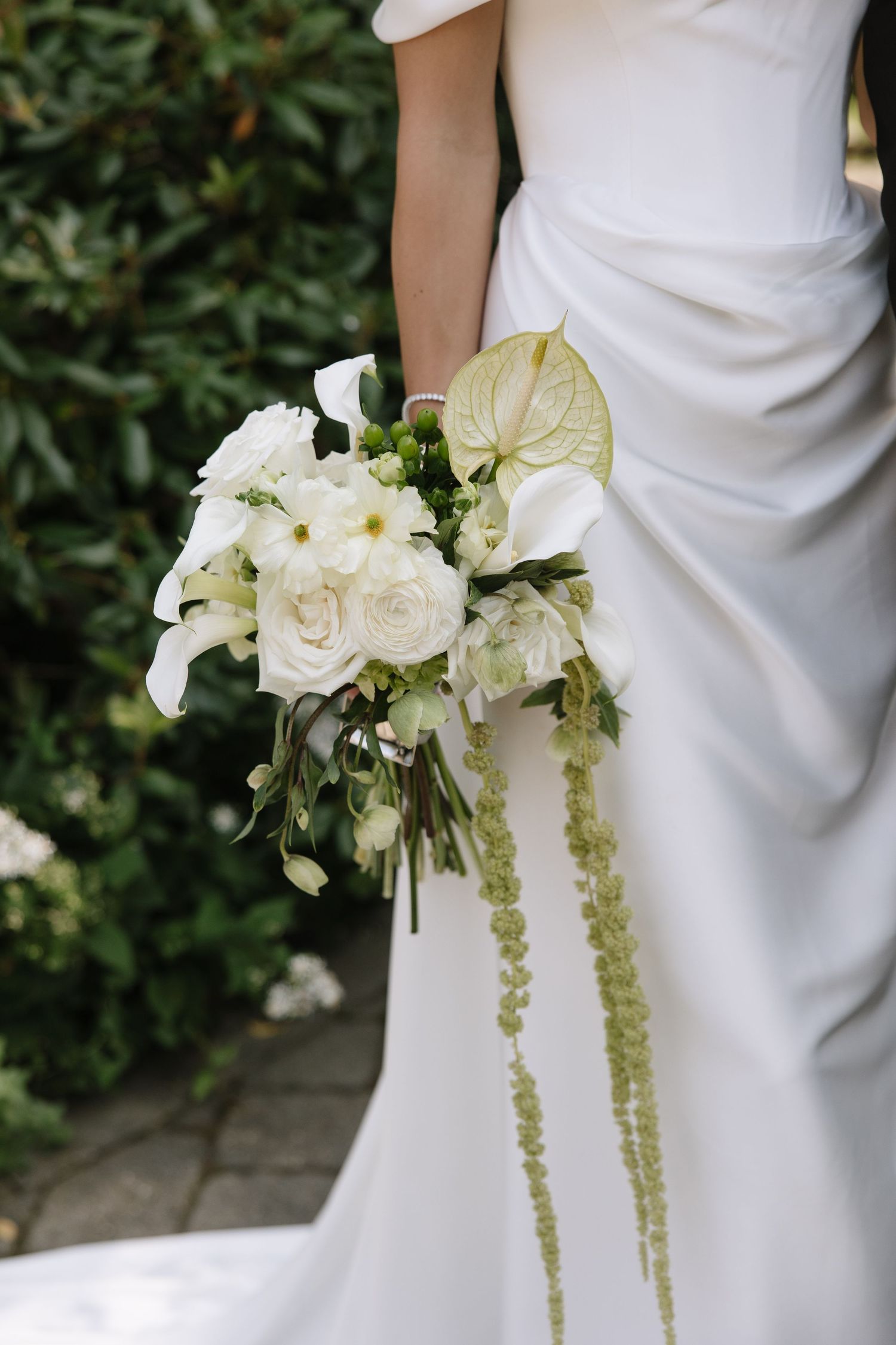 Bride in white gown holding elegant bouquet of white roses, calla lilies, and trailing green amaranthus.