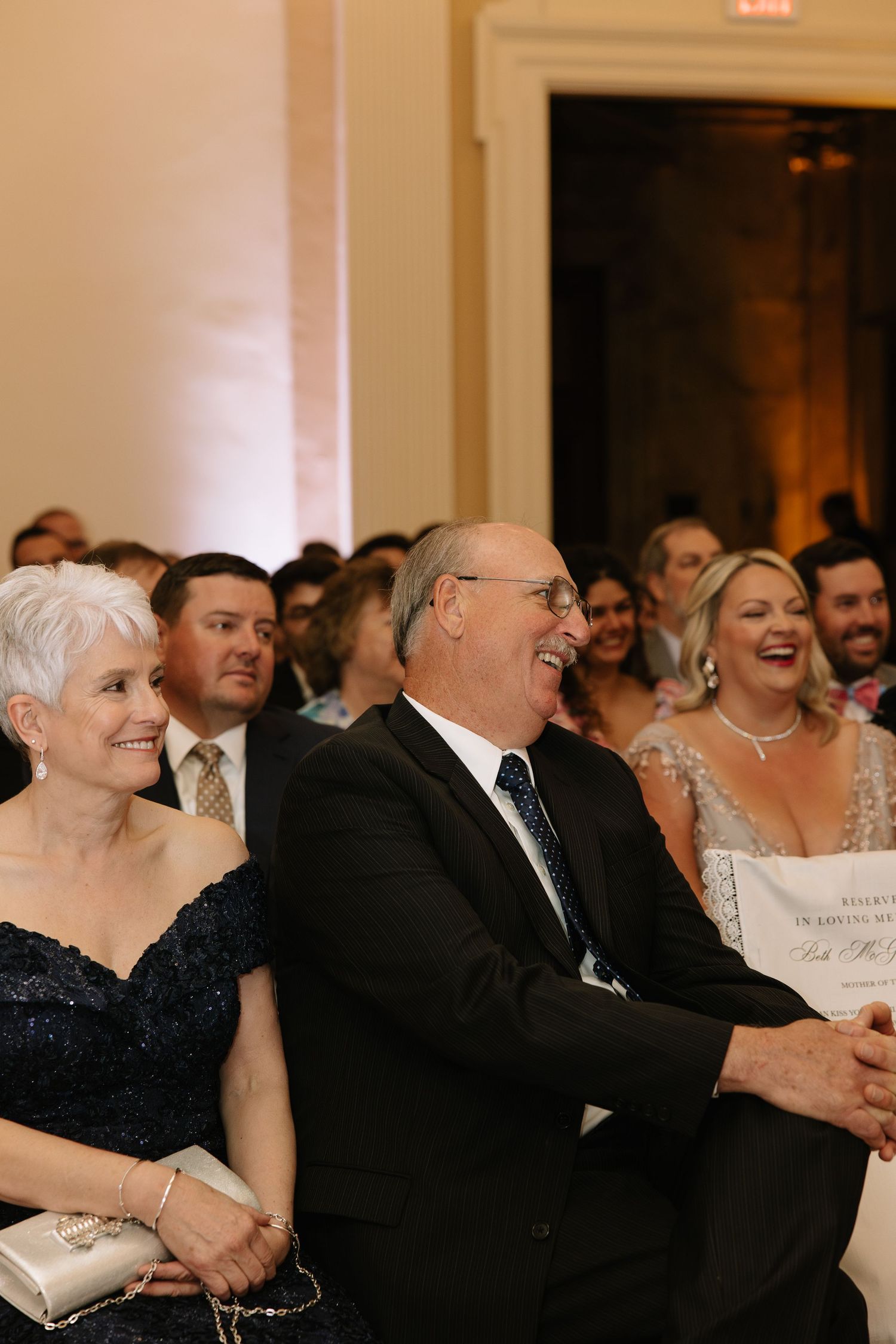Wedding guests laughing and smiling joyfully during ceremony at elegant reception venue.