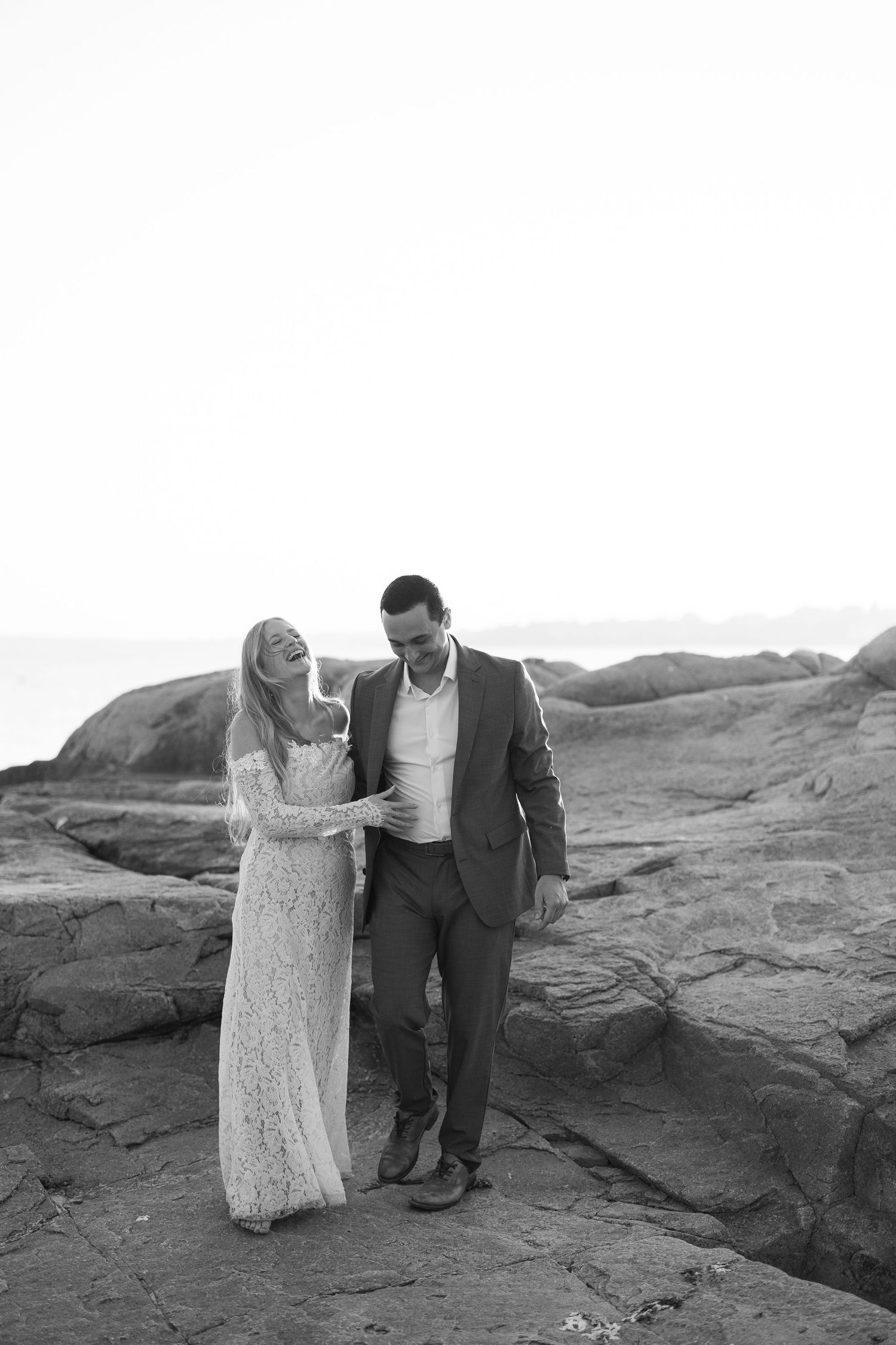 Couple walking along rocky coastline in black and white photography.