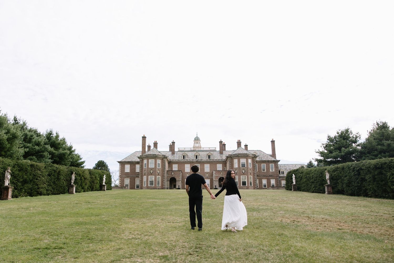 Long distance view of a couple walking towards a grand estate on rolling grounds.