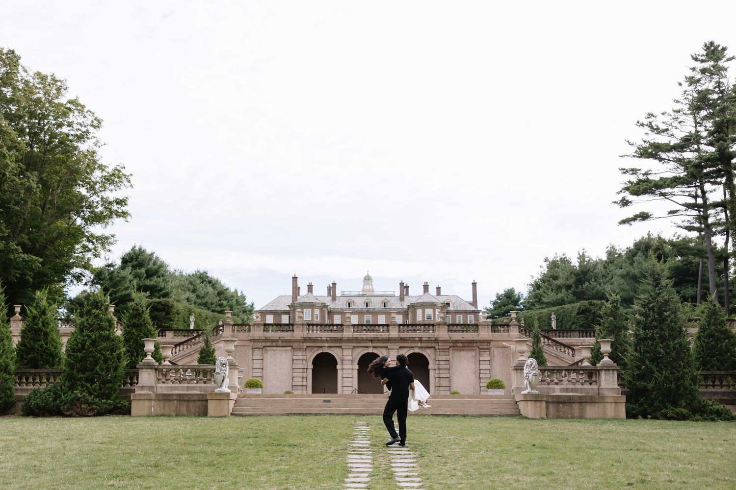 Wide panoramic shot of a historic mansion with classical architecture and landscaped grounds.