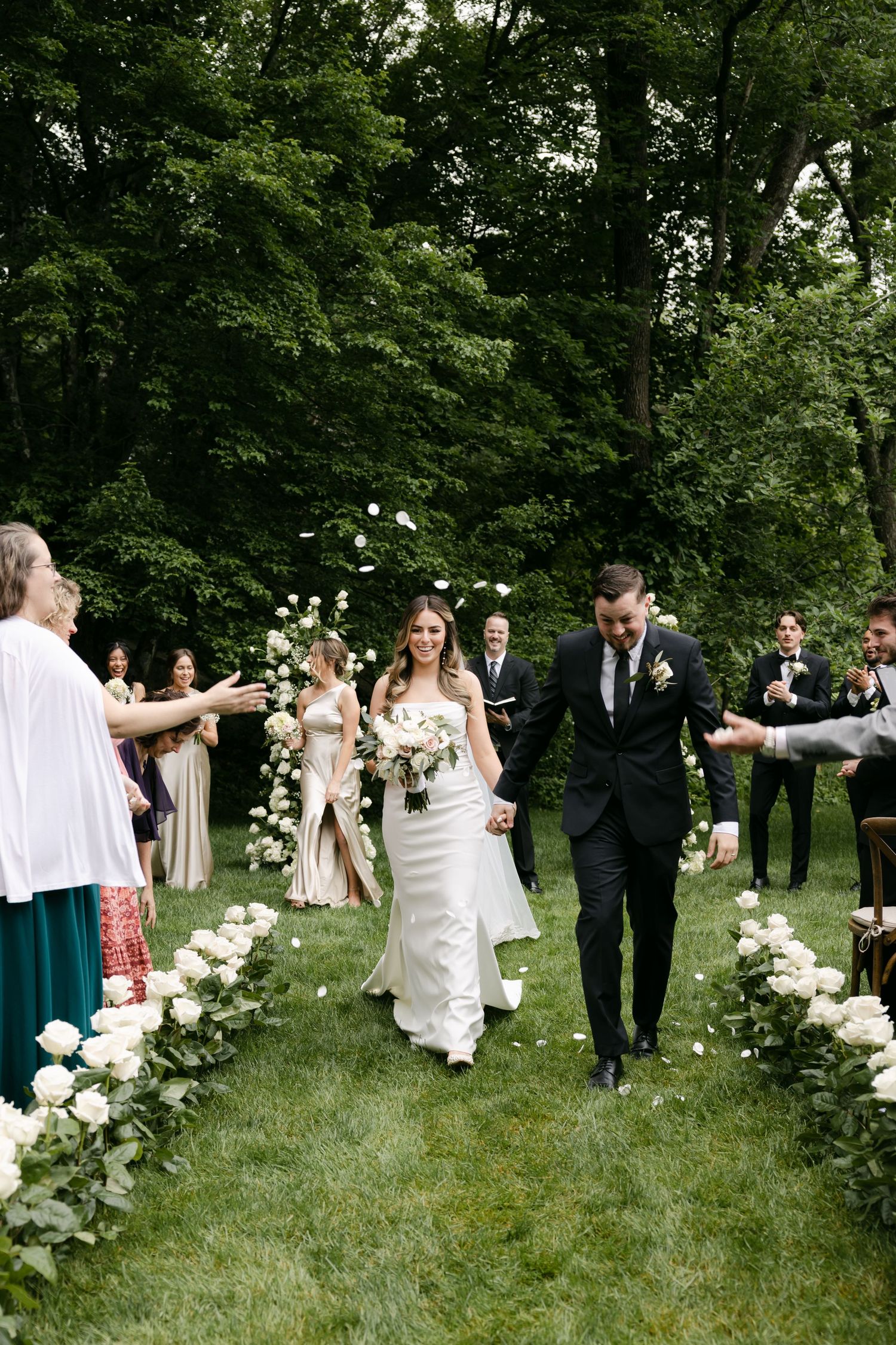 Wedding celebration in a garden setting with guests mingling around white floral arrangements.
