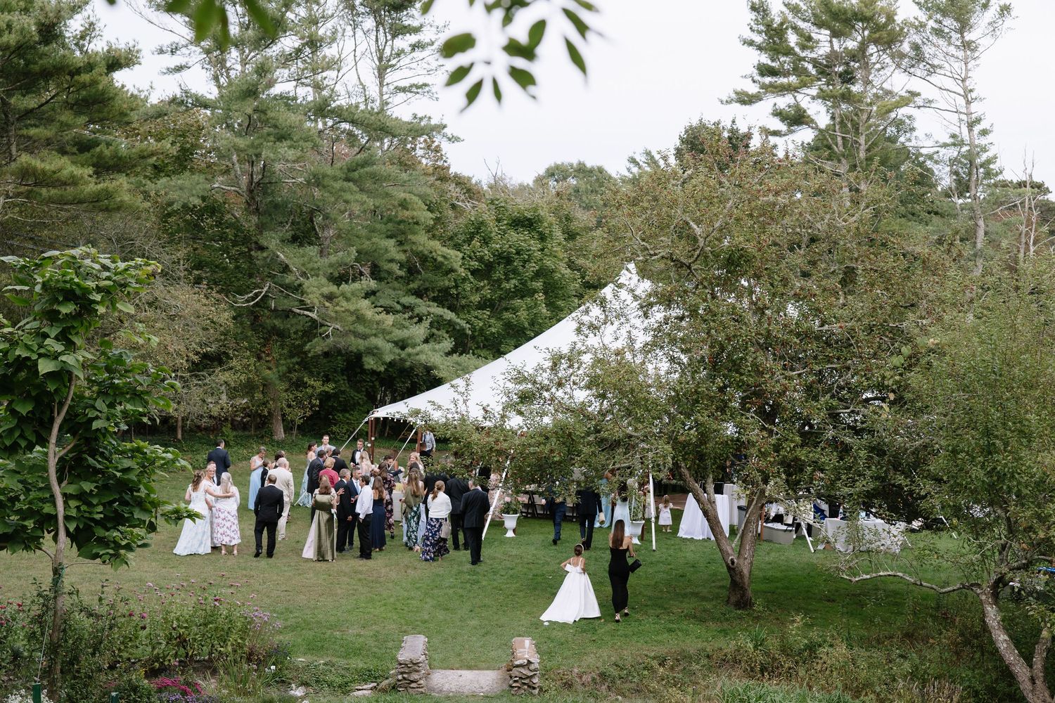 Wide view of an outdoor wedding ceremony setup with guests gathered under trees.