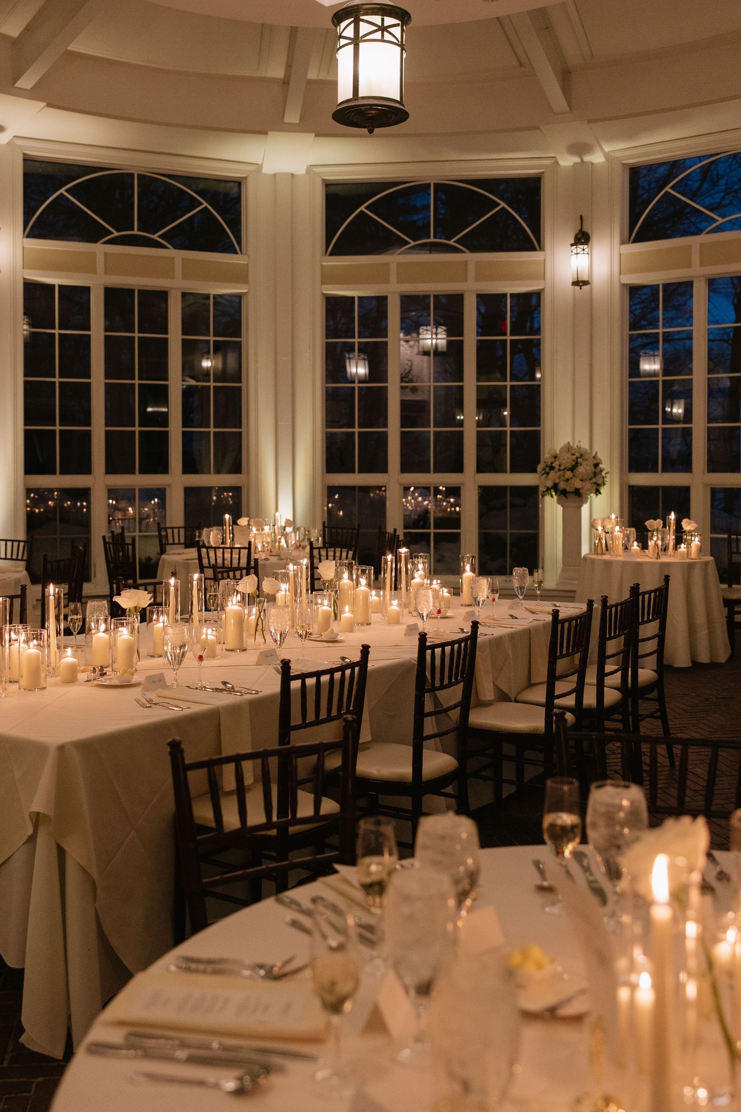 Elegant wedding reception room with candlelit tables and large windows at dusk.