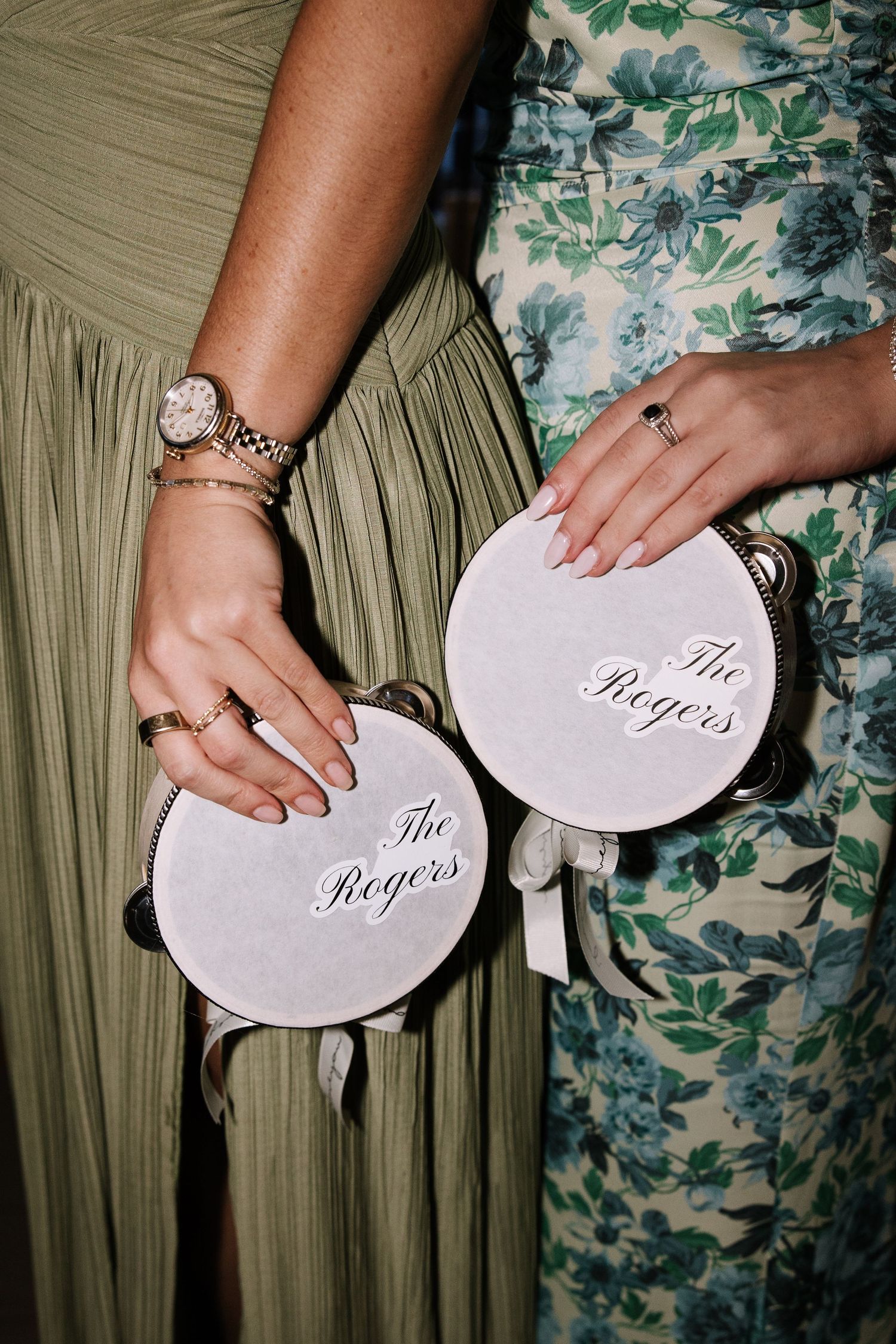 Two women holding personalized white tambourines reading The Rogers at a wedding celebration.