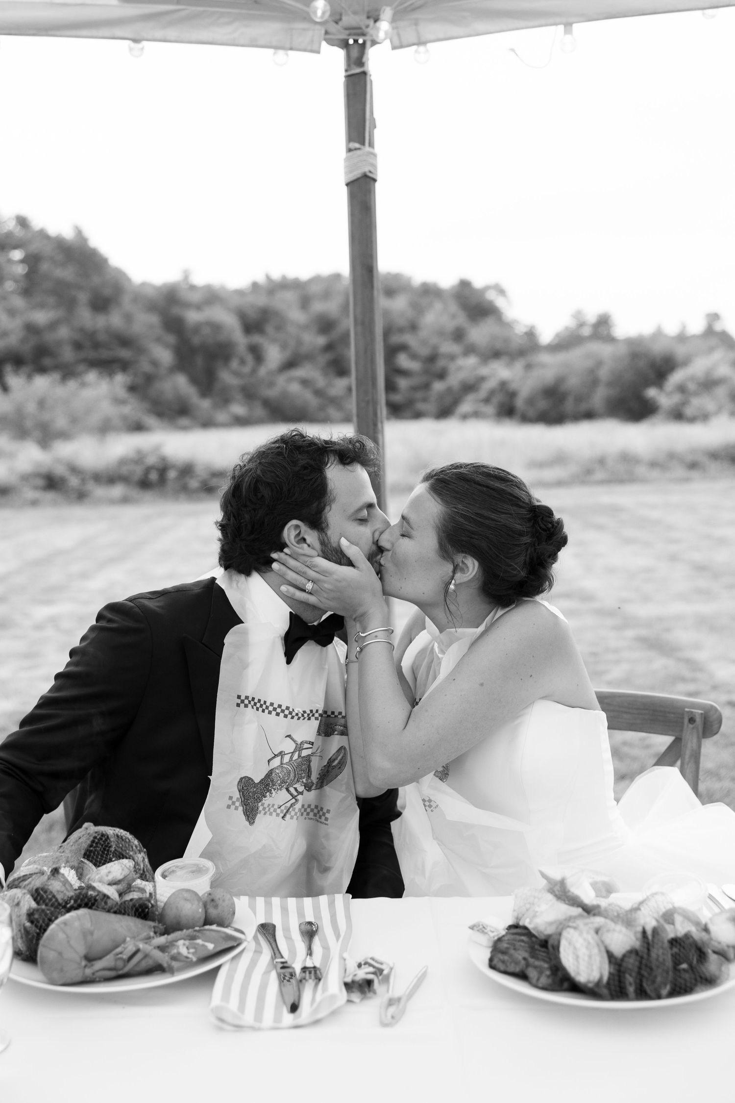 Black and white photo of bride and groom sharing a kiss at their sweetheart table during wedding reception.