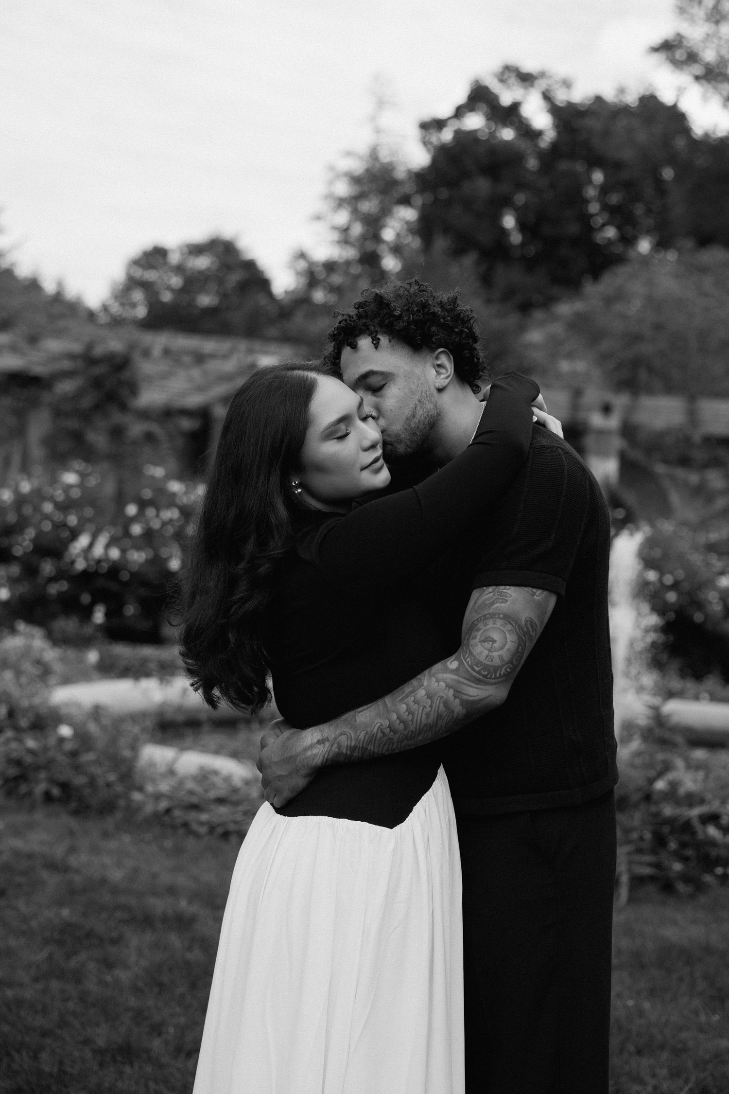 A romantic moment captured between two people in black and white against a garden backdrop.