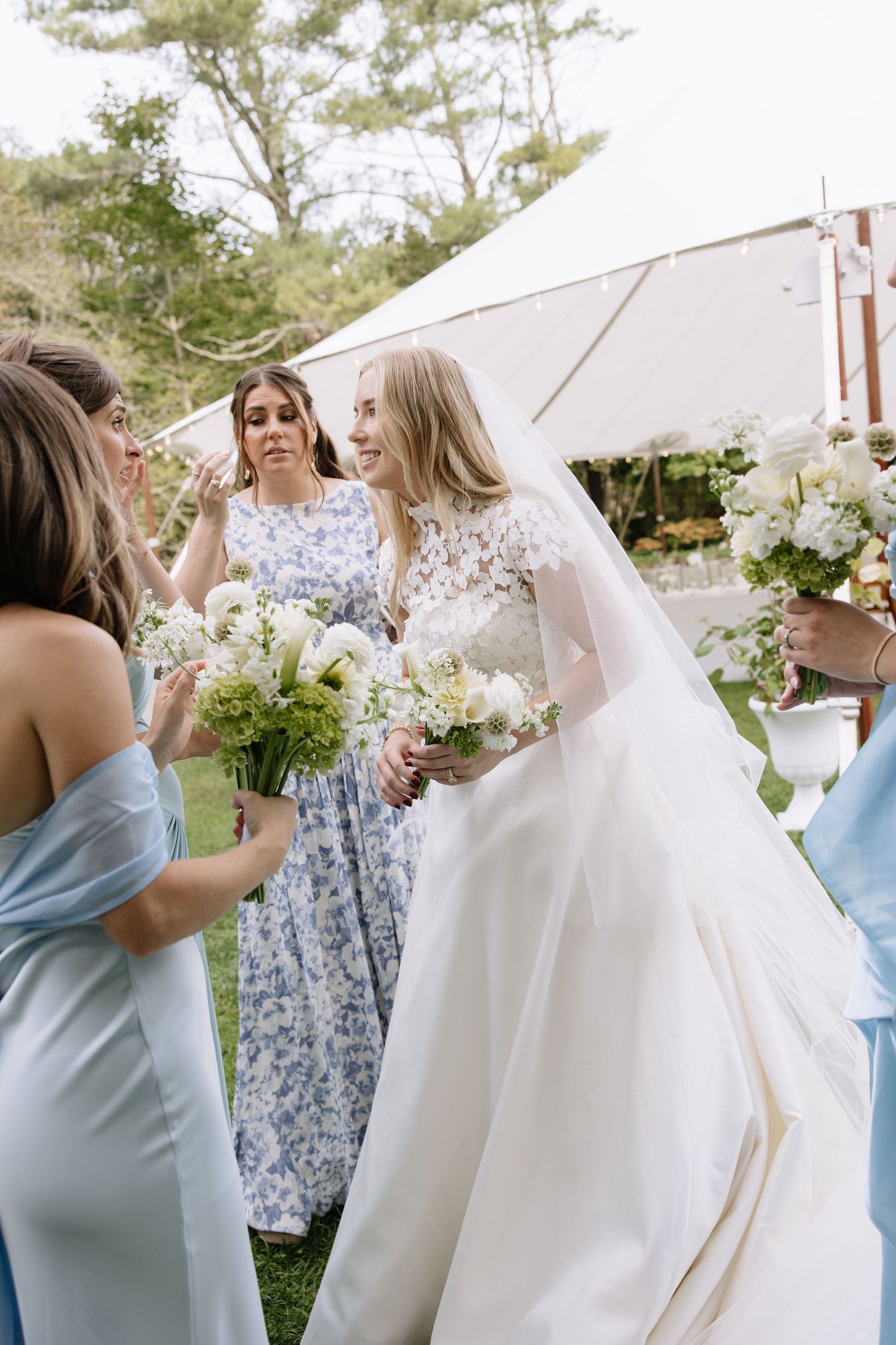 A bride in a white gown shares a moment with her bridesmaids under a wedding tent.