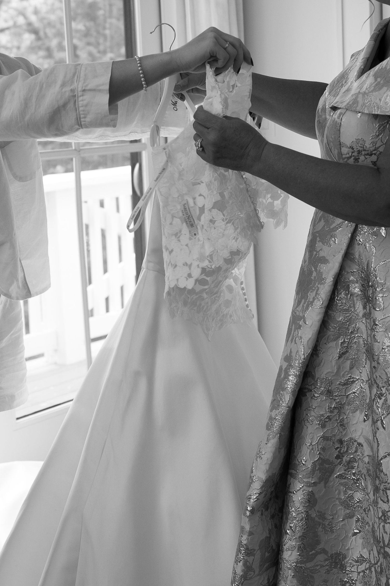 Wedding dresses with intricate lace details hanging by windows in preparation.