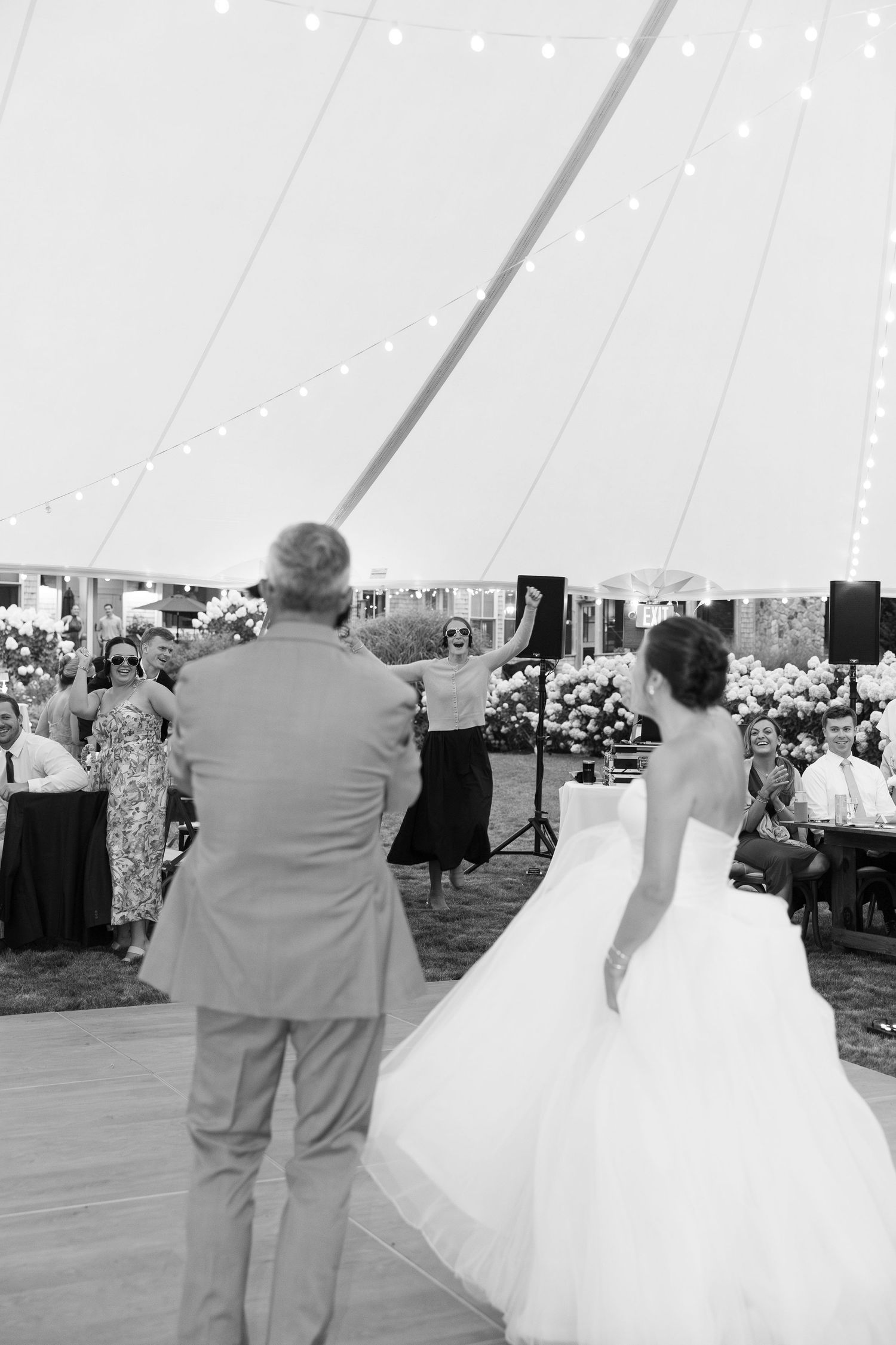 Bride in white gown shares first dance with father under string lights inside elegant wedding tent.