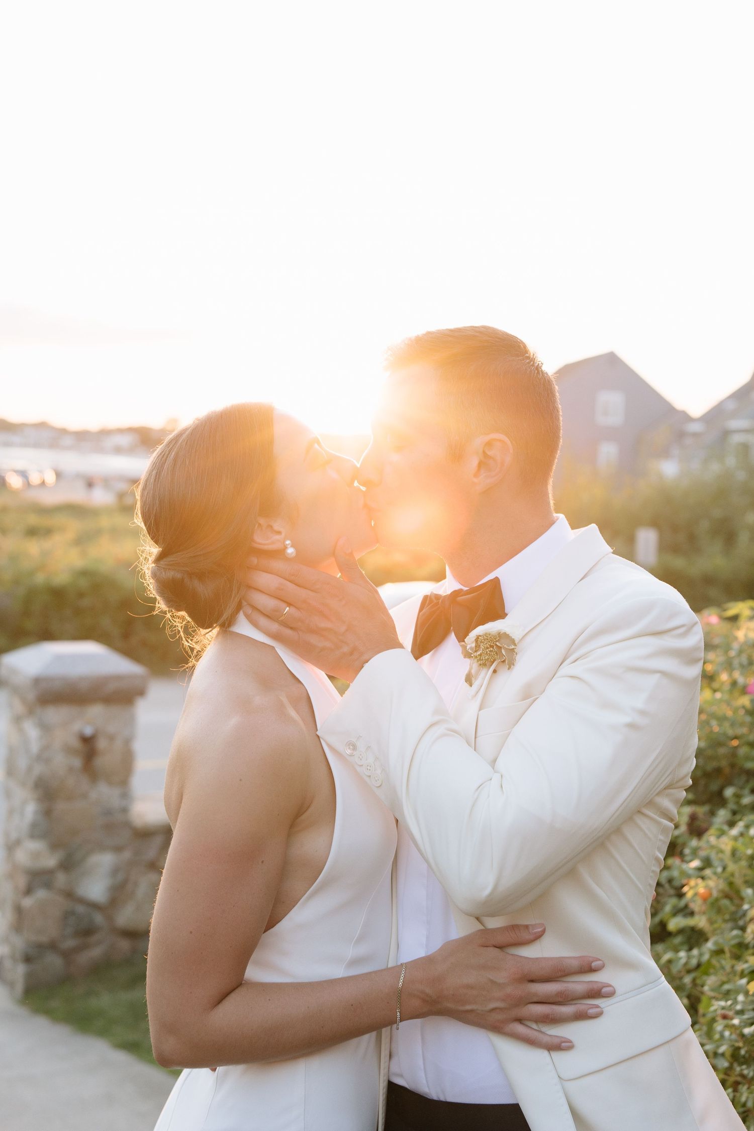 Bride and groom share a romantic kiss at golden hour sunset during their outdoor wedding ceremony.