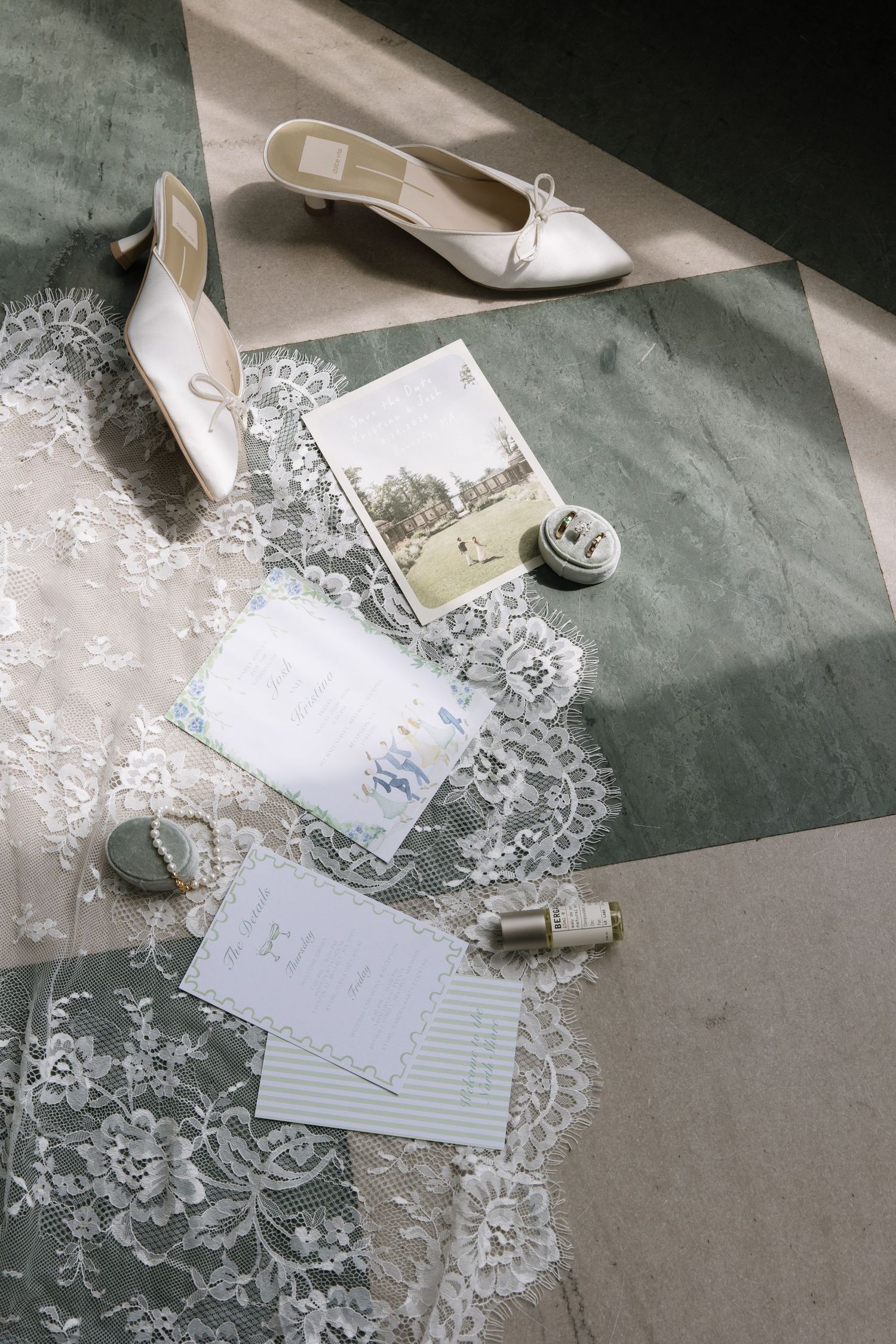 Flat lay of bridal accessories including lace veil, heels, invitations, and ribbons on tiled floor.