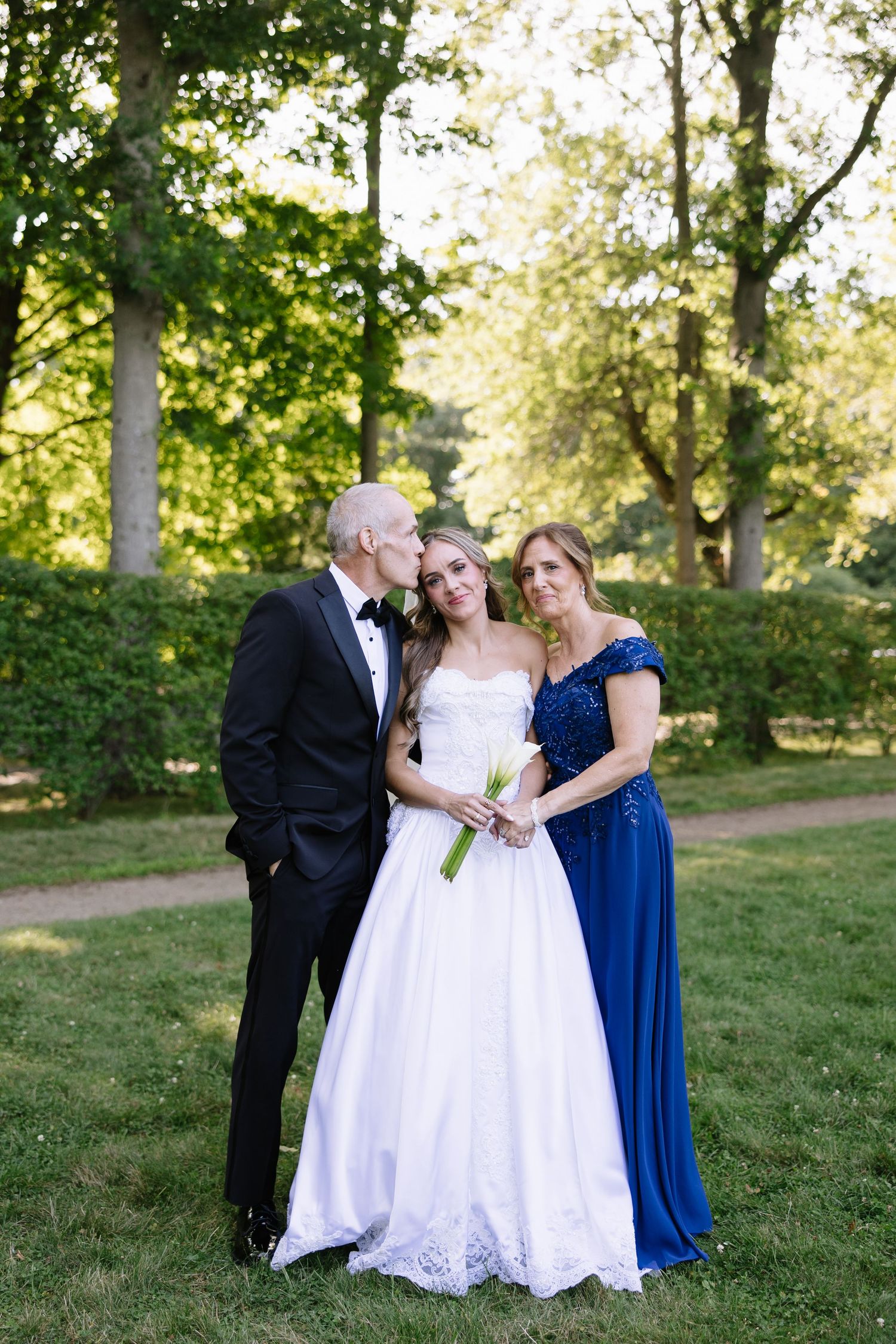 Wedding portrait on green lawn with formal attire including white gown and navy dress.