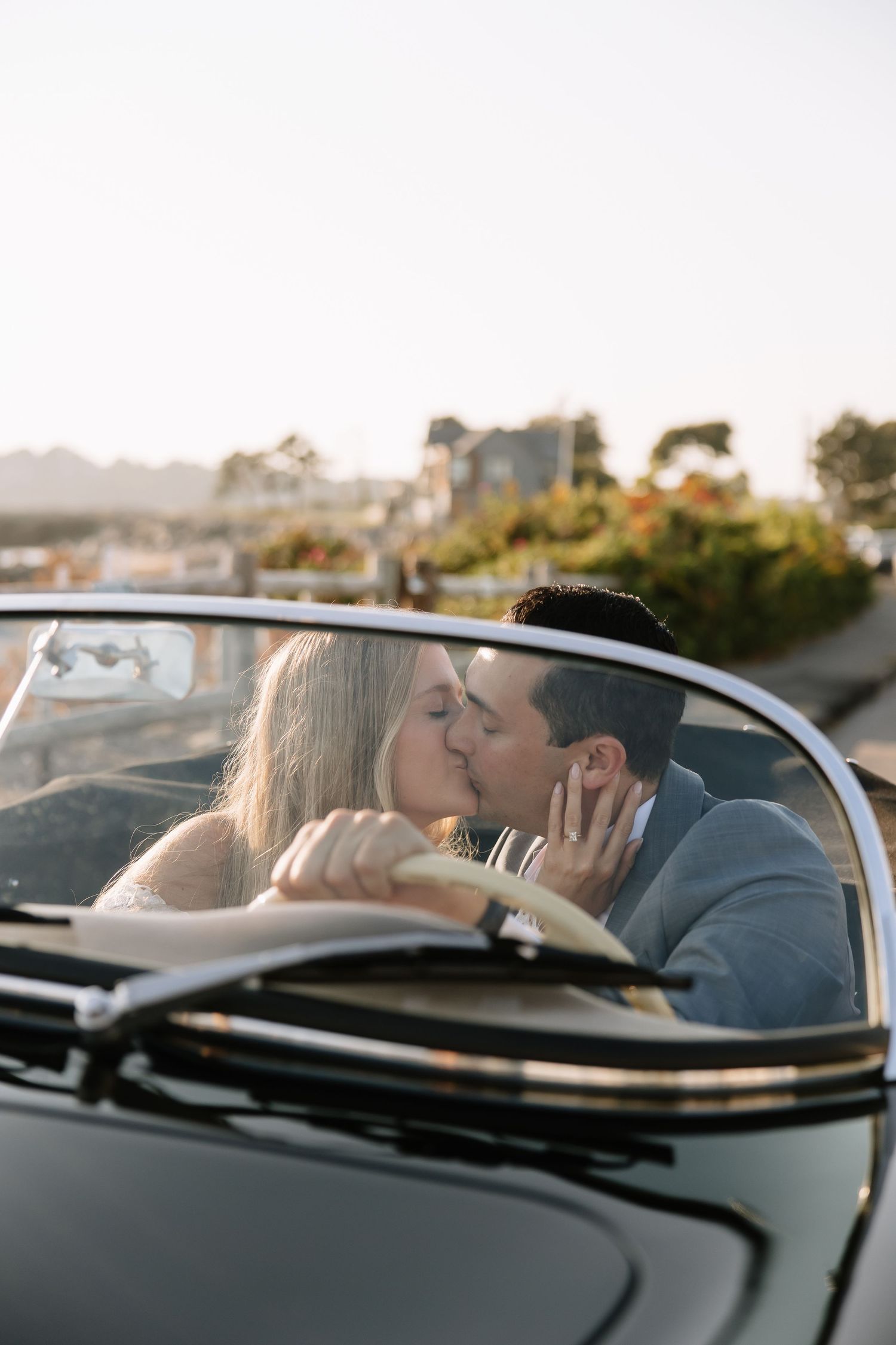 A couple embraces in the front seat of a classic convertible car at sunset.