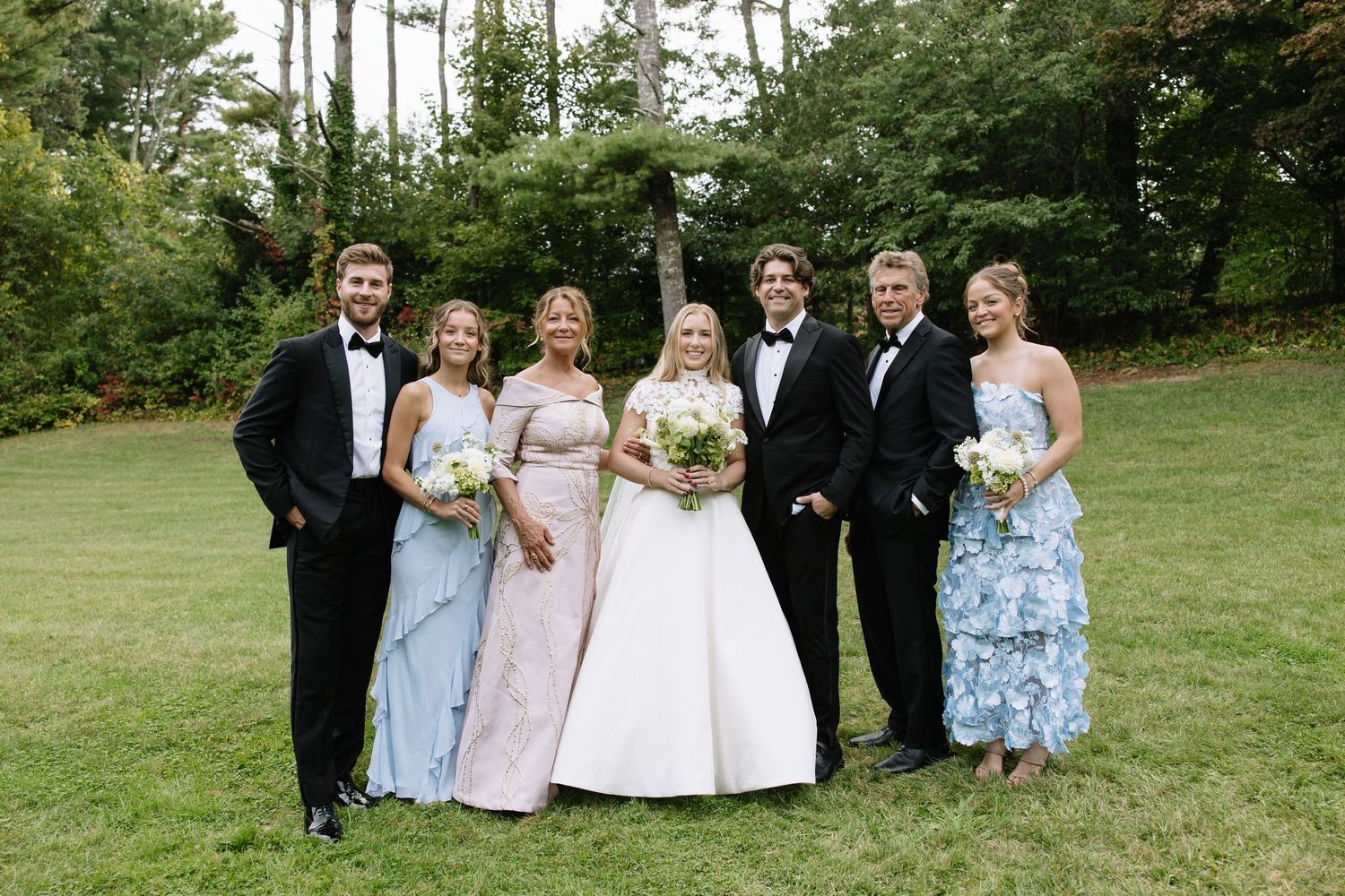 Wedding party members lined up for formal group photos on a grassy lawn.