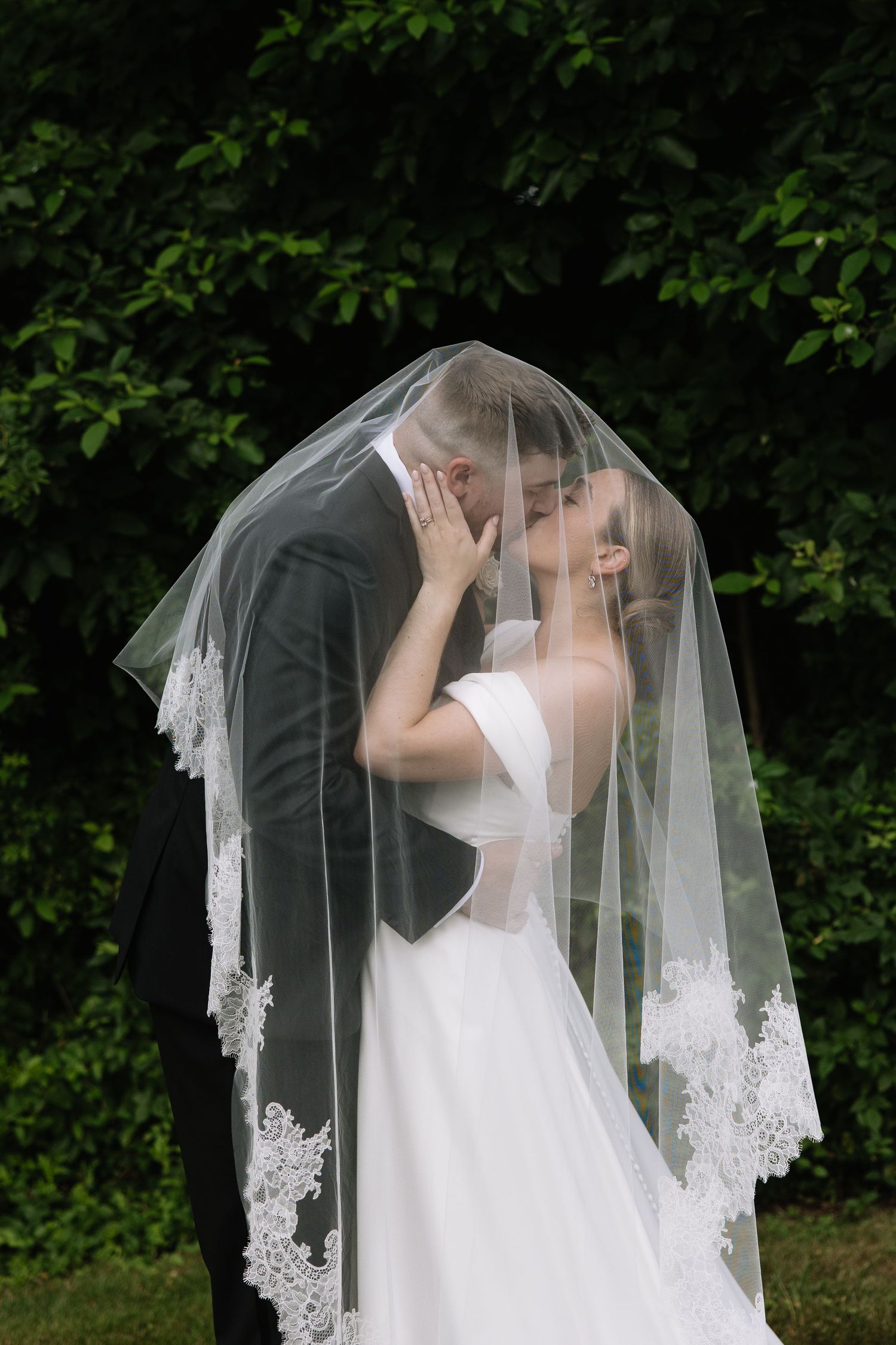 Wedding couple sharing intimate moments under a delicate lace veil in a garden setting.
