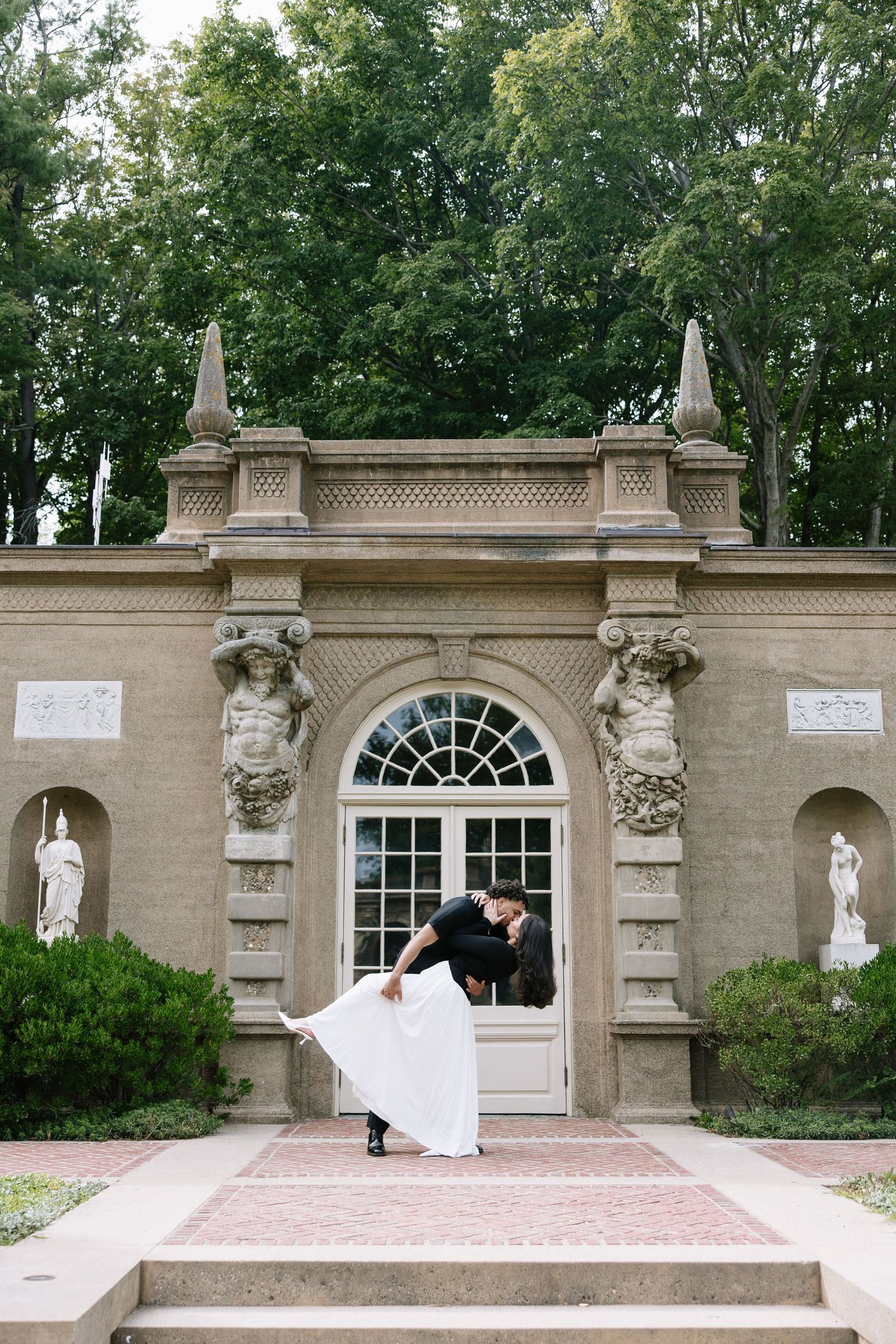 A romantic dip pose in front of an ornate classical doorway with statues and architectural details.