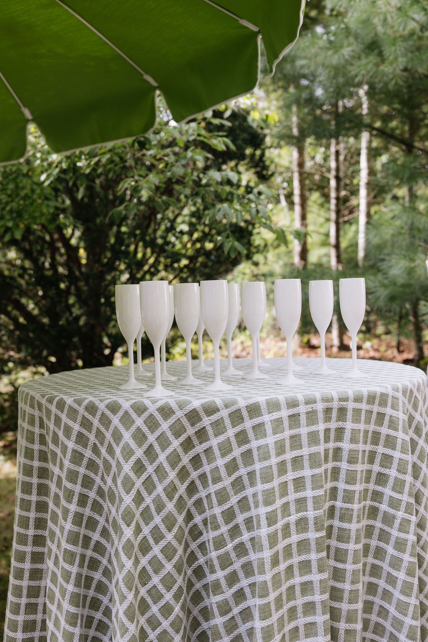 White champagne glasses lined up on patterned tablecloth at outdoor event.