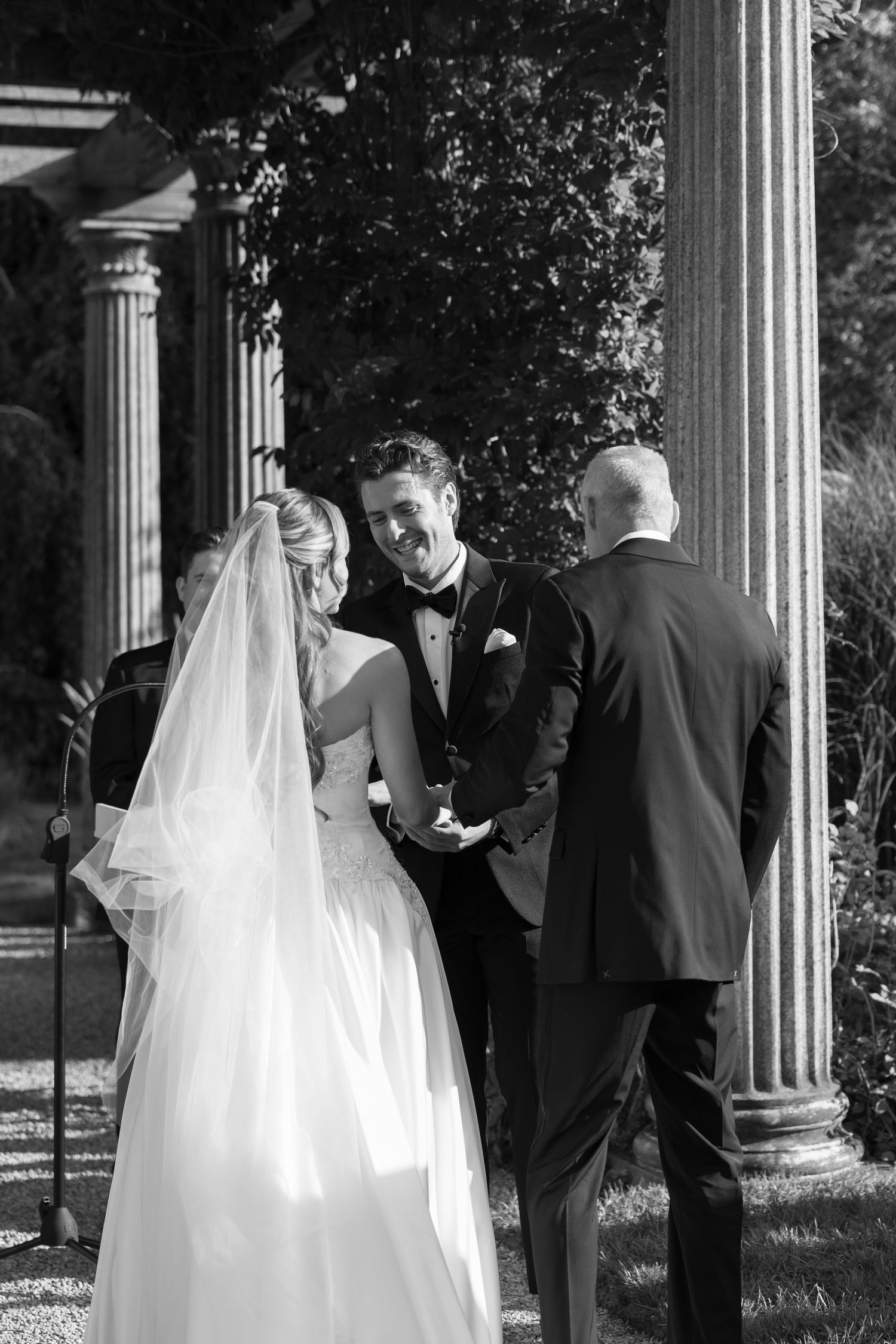 Wedding couple shares intimate moment among classical columns in black and white.
