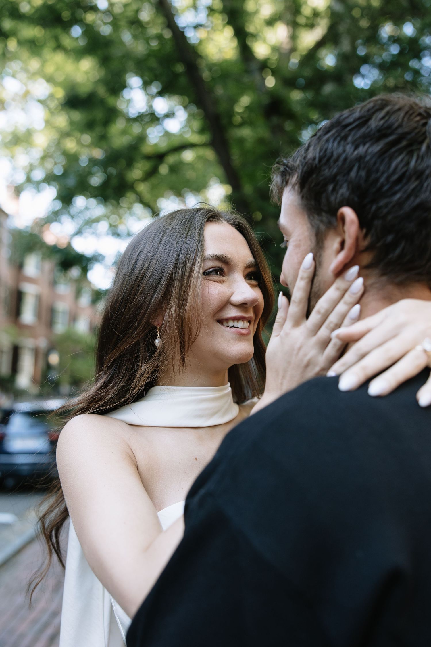 A tender moment captured between a couple on a tree-lined city street.