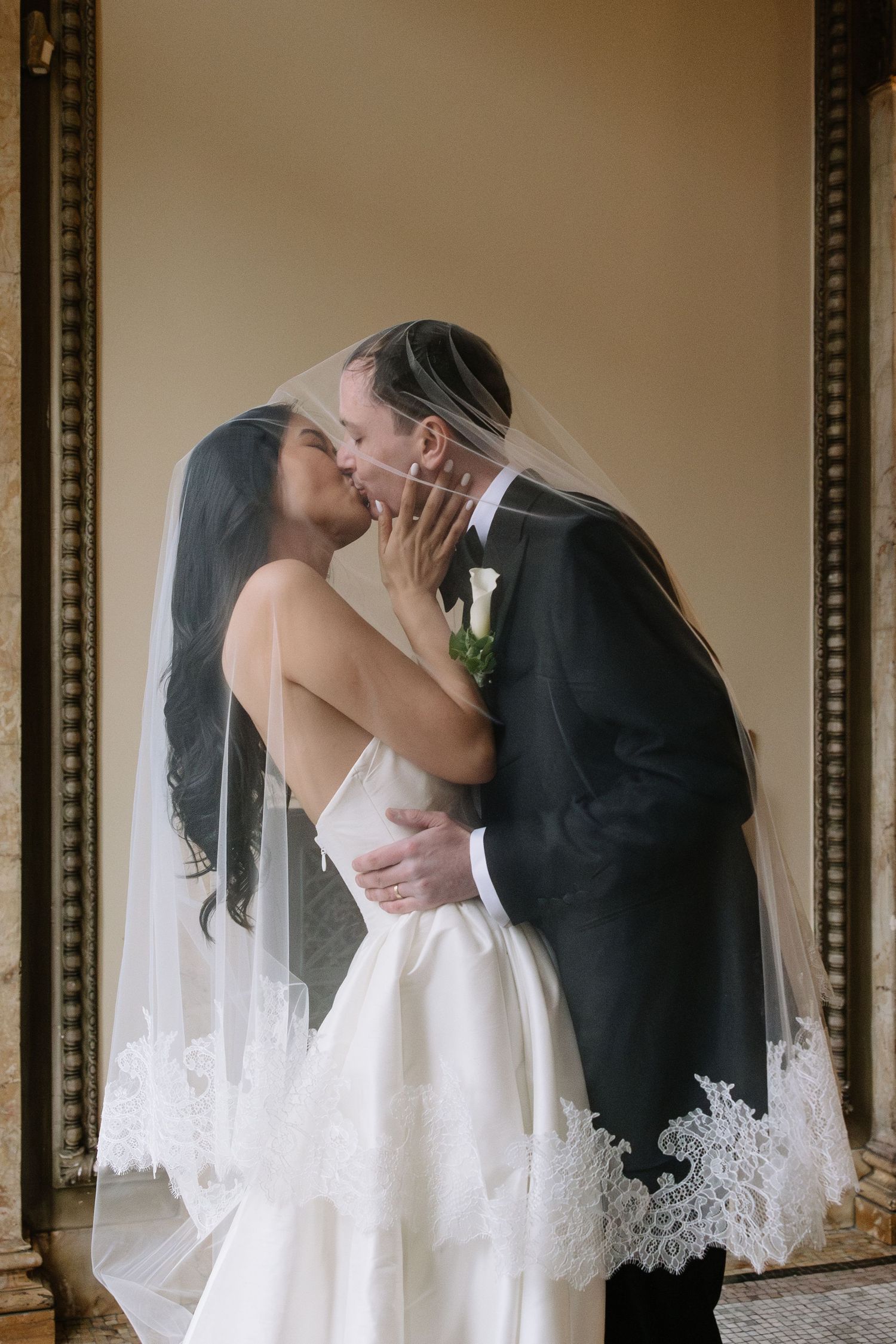 Bride and groom sharing romantic kiss under lace-trimmed veil at wedding ceremony.