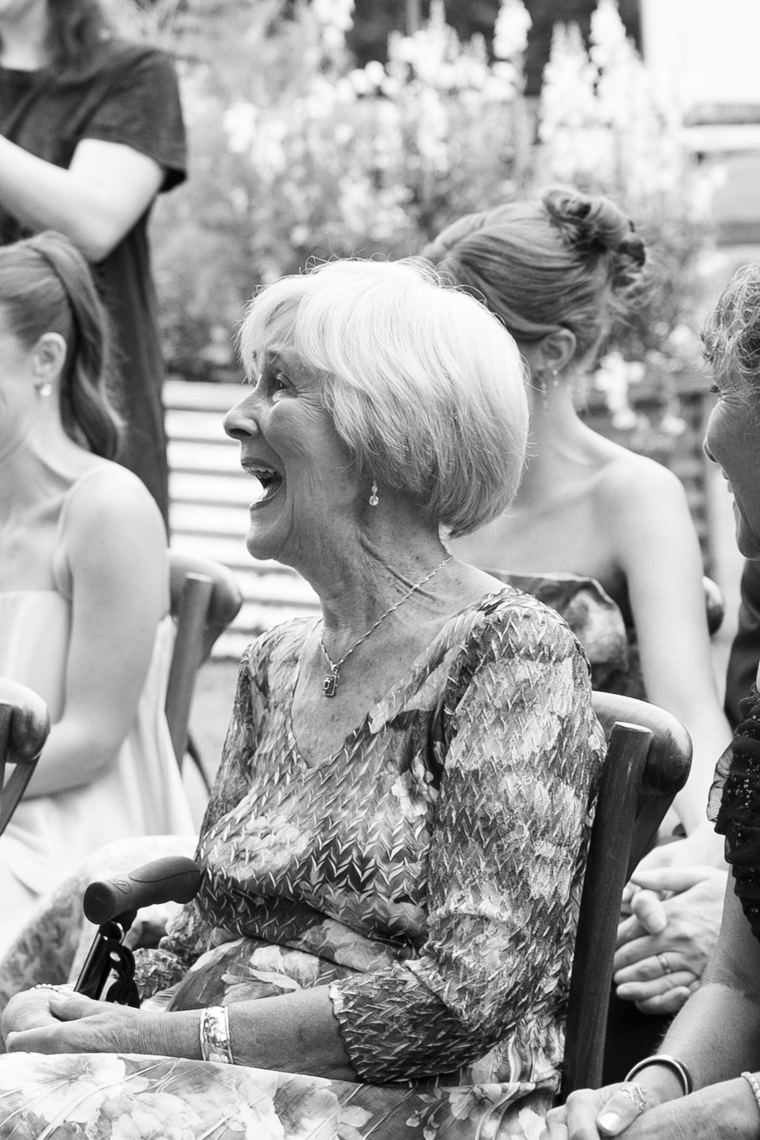 Elderly woman laughing joyfully at outdoor gathering, black and white photo.