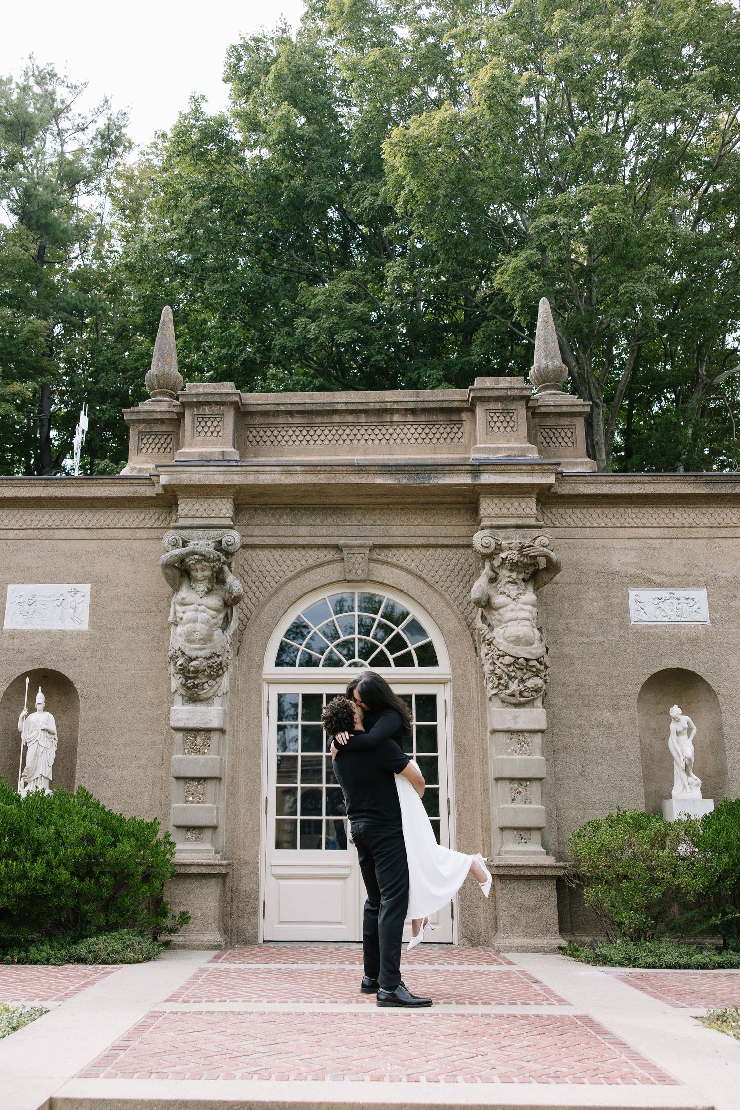 A dramatic lift pose in front of a neoclassical entrance with decorative columns and statues.