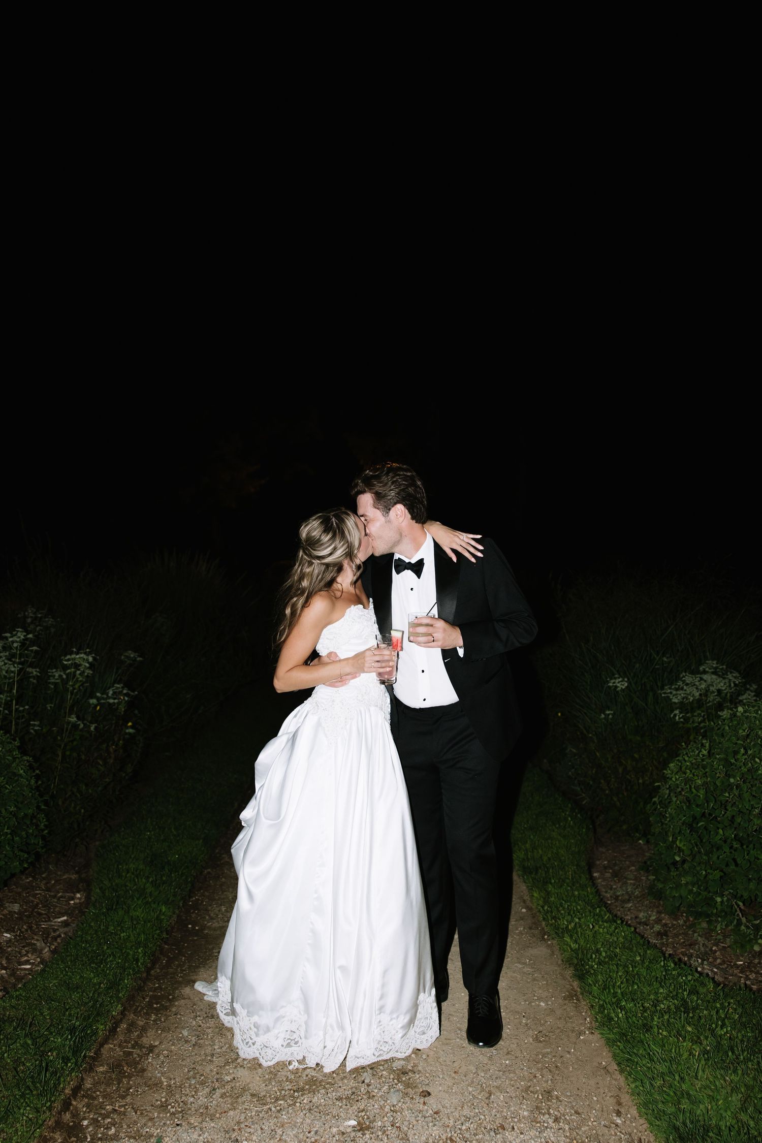 A couple walks together on a dark path at night during their wedding celebration.