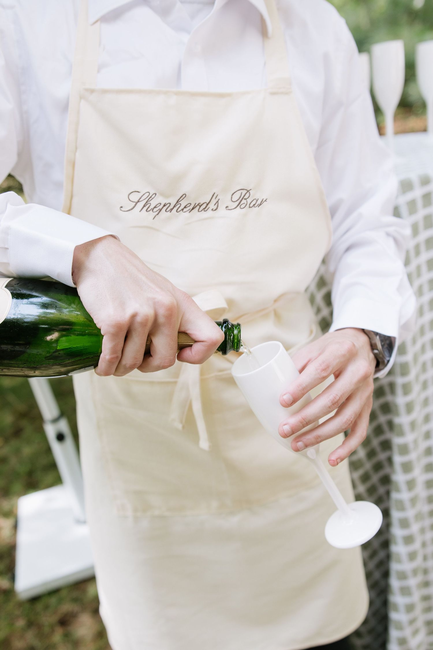 Hands opening champagne bottle while wearing white apron.