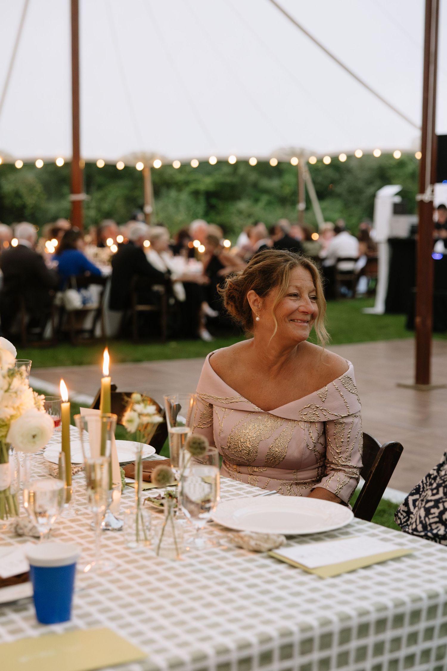 Wedding reception table settings with glowing candles and elegant place settings under a tent.