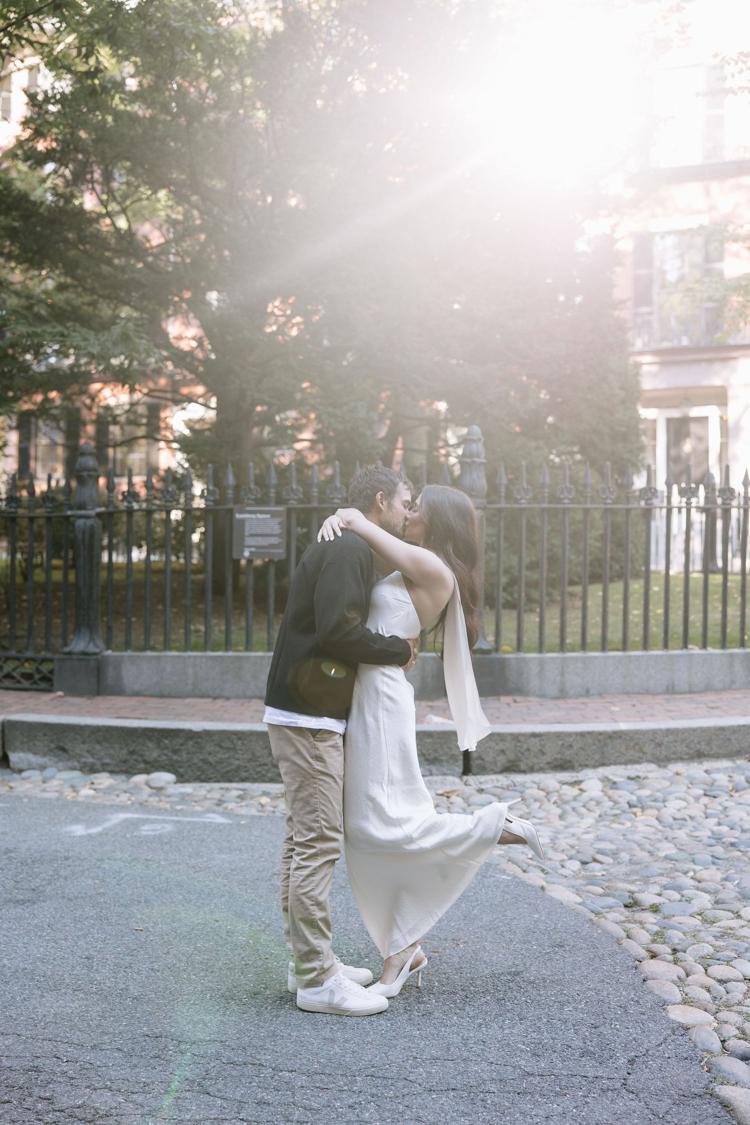 Couple sharing a romantic embrace on a sunlit cobblestone street.