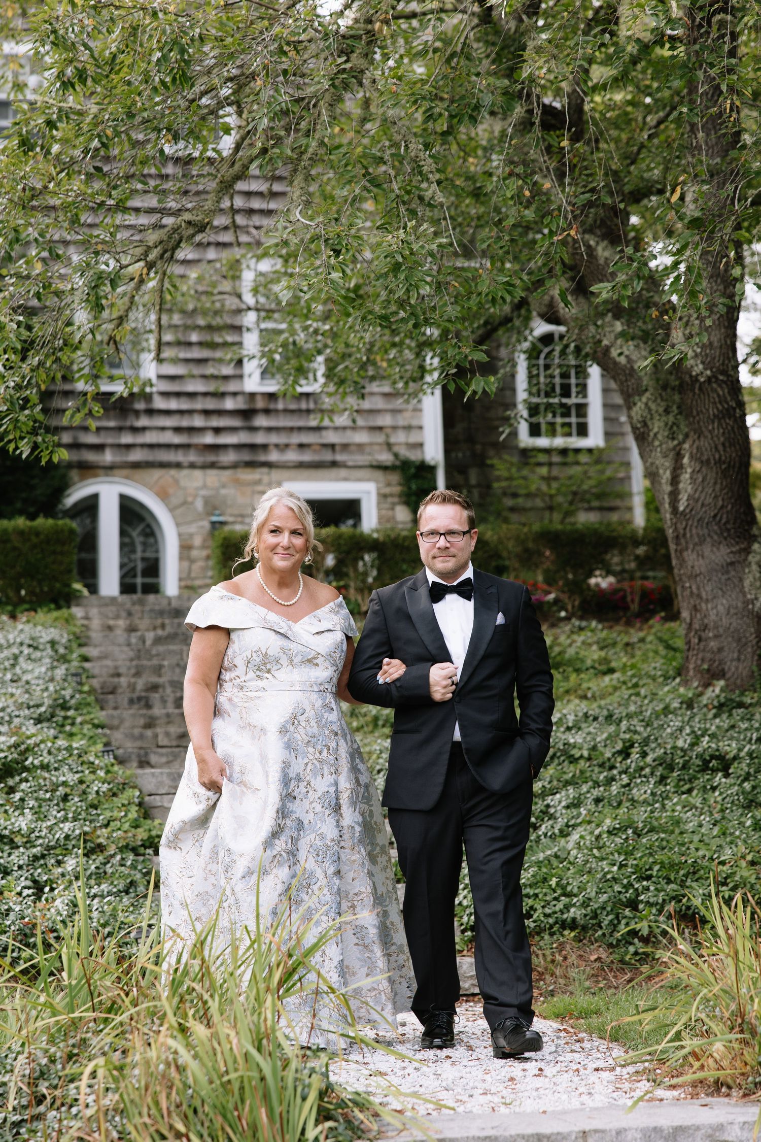 Couple walking together on a stone path surrounded by trees and landscaping.
