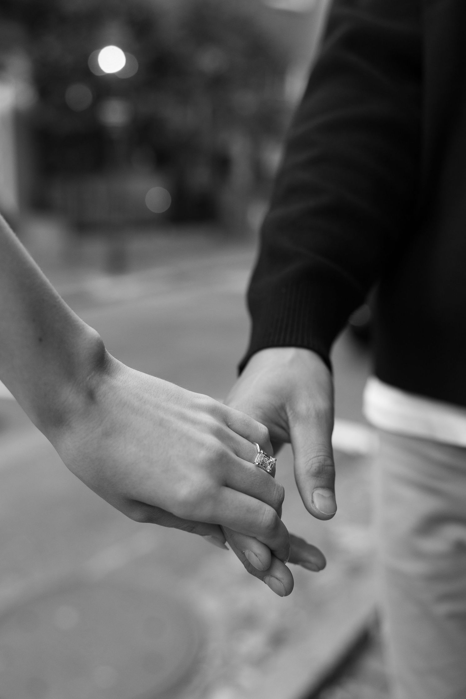 Close-up black and white photo of hands holding with an engagement ring visible.